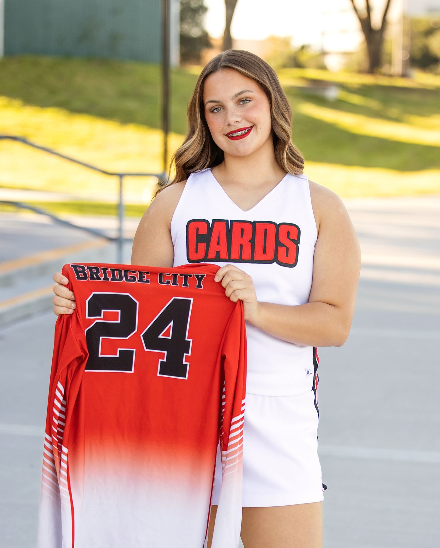 A person in a white top displays a red sports jersey with number 24 against an outdoor background.