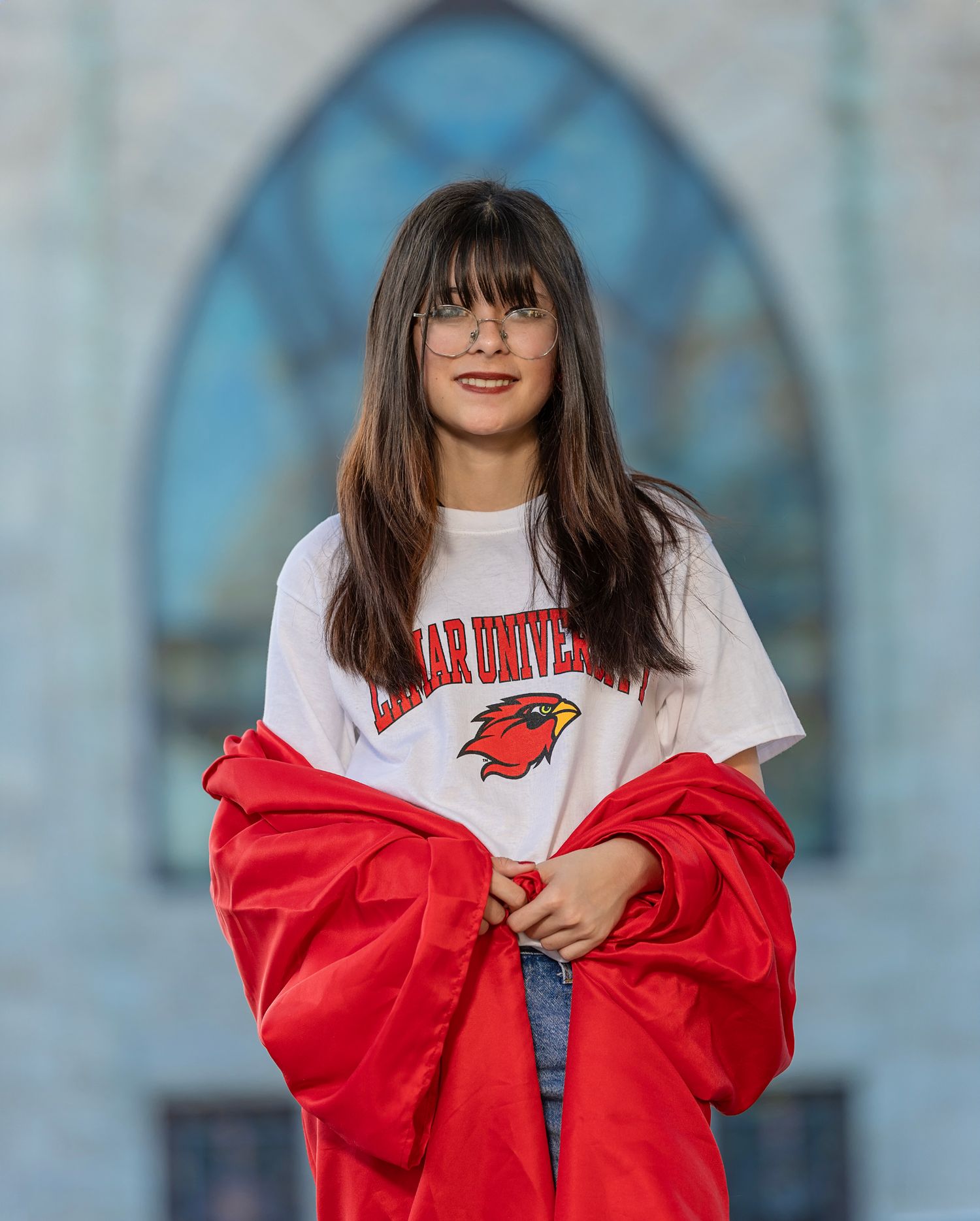 Person wearing a white t-shirt and red jacket poses against a blurred blue background.