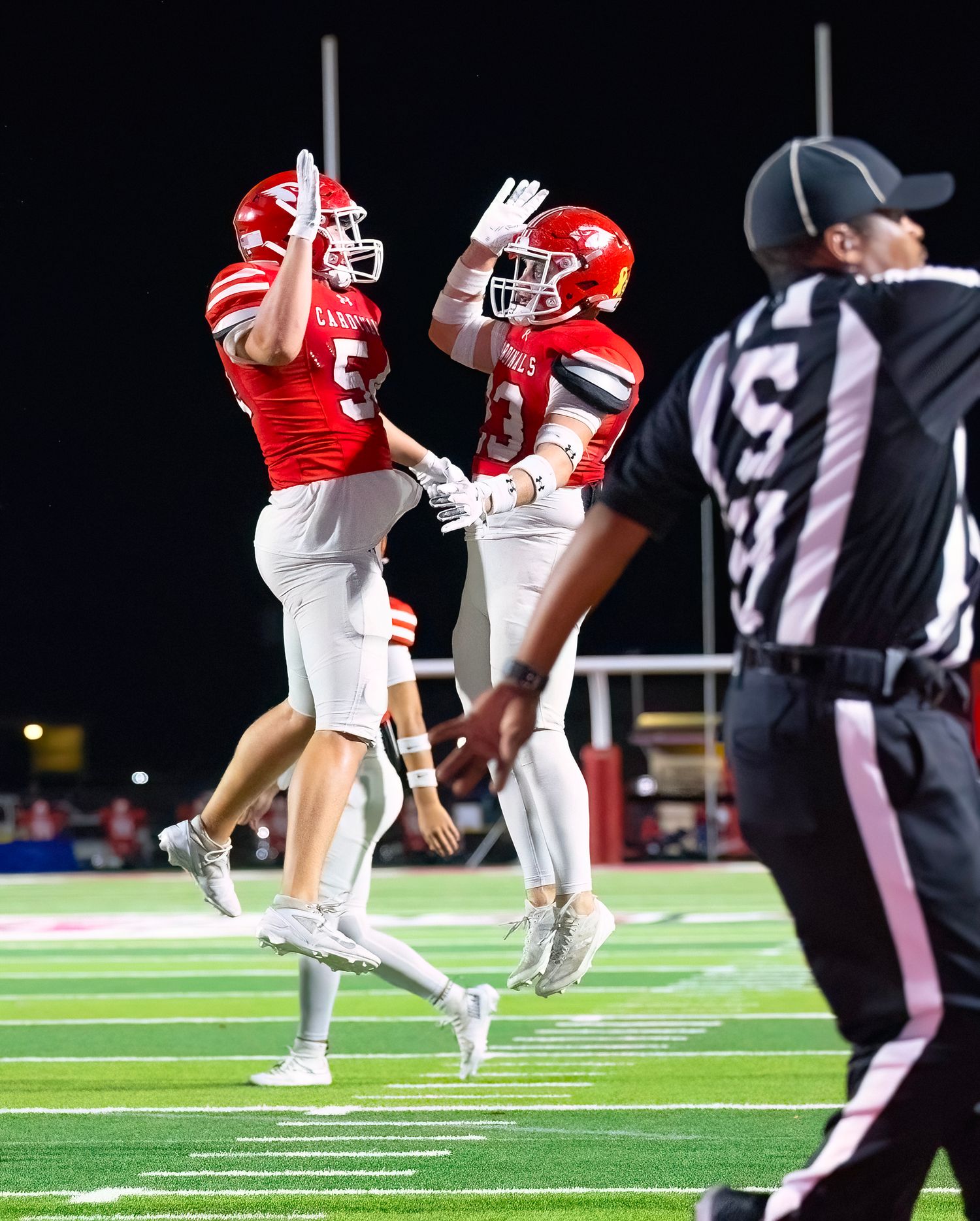 Action Photography with Two football players in red uniforms celebrate by jumping and chest bumping on the field.