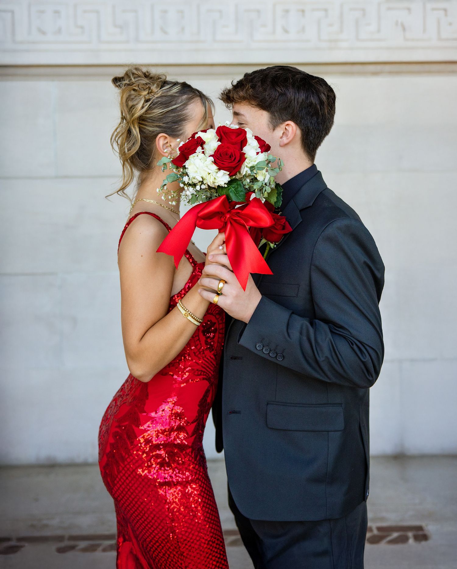 A couple in formal attire share an intimate moment, with the woman wearing a stunning red sequin dress.