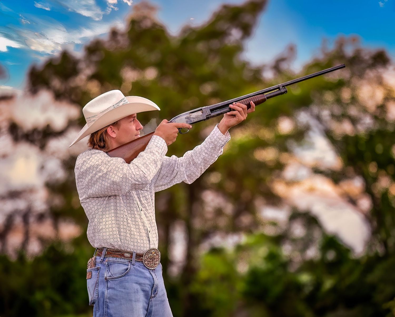 Hunter in plaid shirt and jeans aims shotgun while clay target shooting against blurred outdoor background.