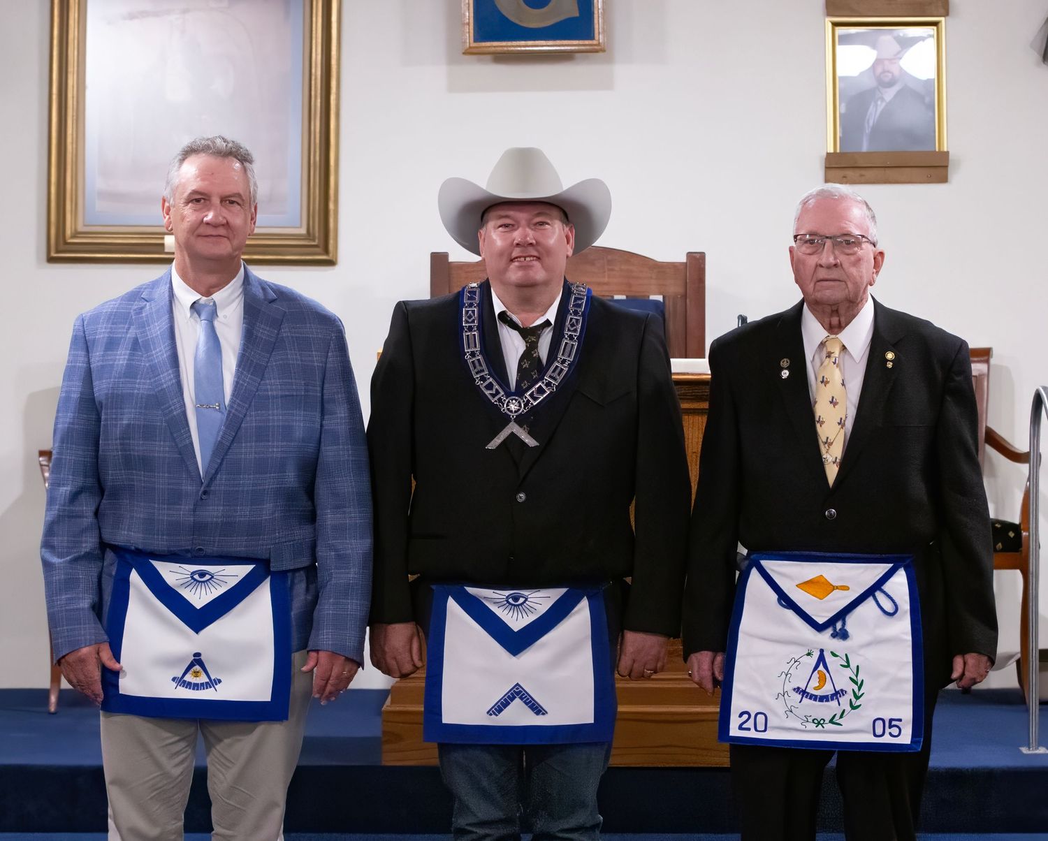 Masonic Installation event row of people wearing masonic aprons and formal attire stand together in what appears to be a lodge meeting room.