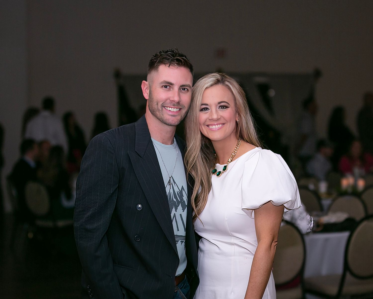 Christmas party event with couple in formal attire smiles and poses together at what appears to be a wedding reception or formal event.