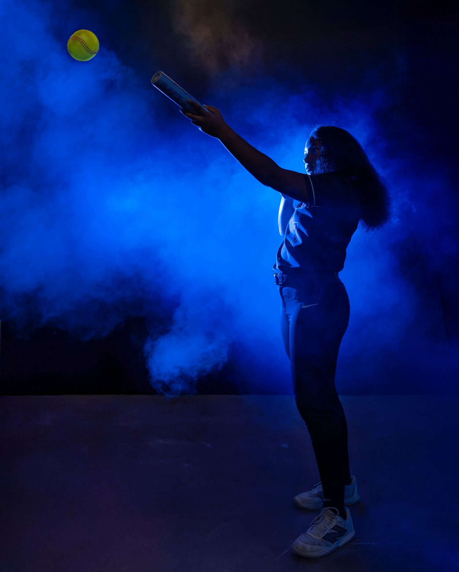 Silhouetted figure reaching up to catch a tennis ball against a dramatic blue backlit background with smoke effects.