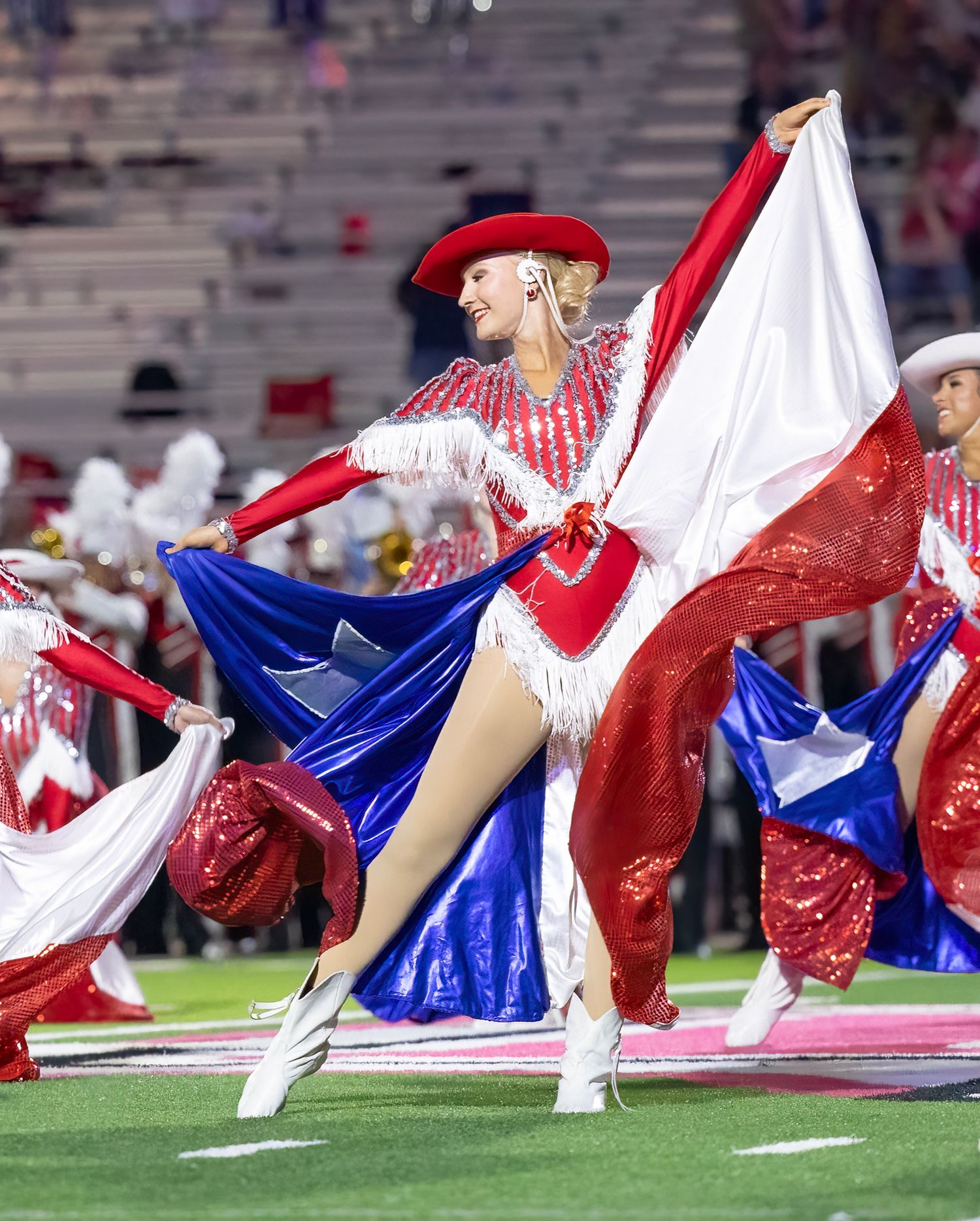 Dance team performs choreographed moves in red, white and blue costumes on the field.