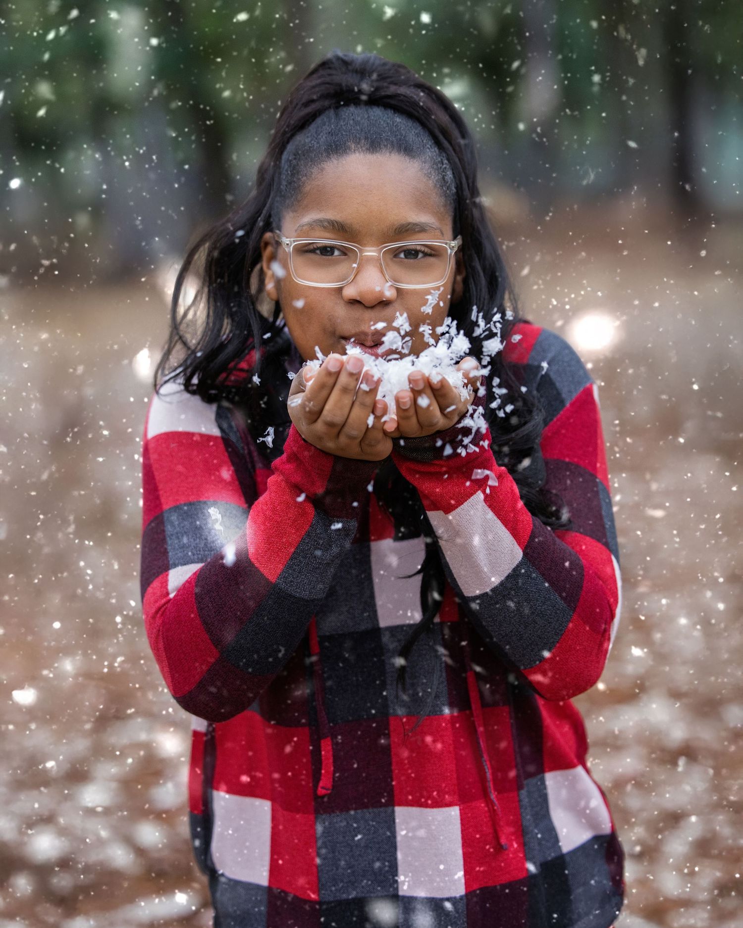 Someone in buffalo plaid jacket blowing snow in a playful winter scene.