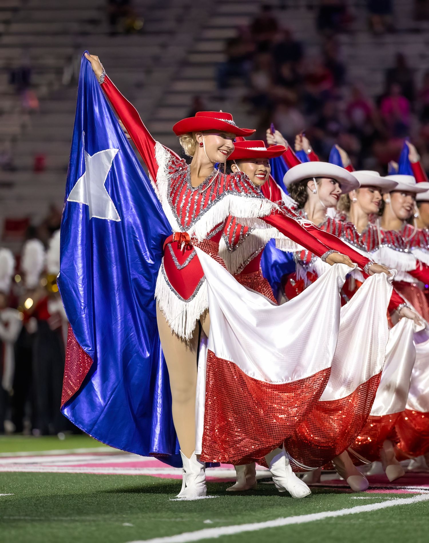 Strutters  Drill Team perform Texas Skirt Dance  in red and white uniforms hold Texas state flag during halftime show.