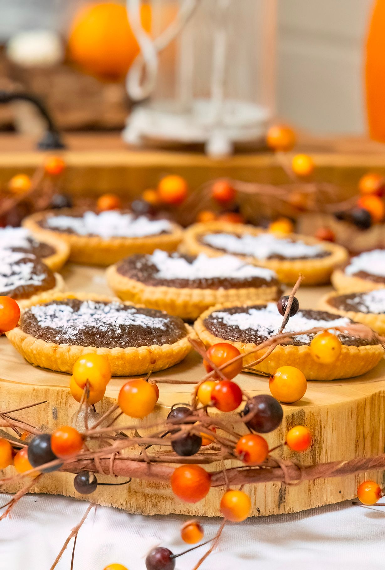 Chocolate tarts decorated with powdered sugar displayed on wooden board with orange berries and twigs.