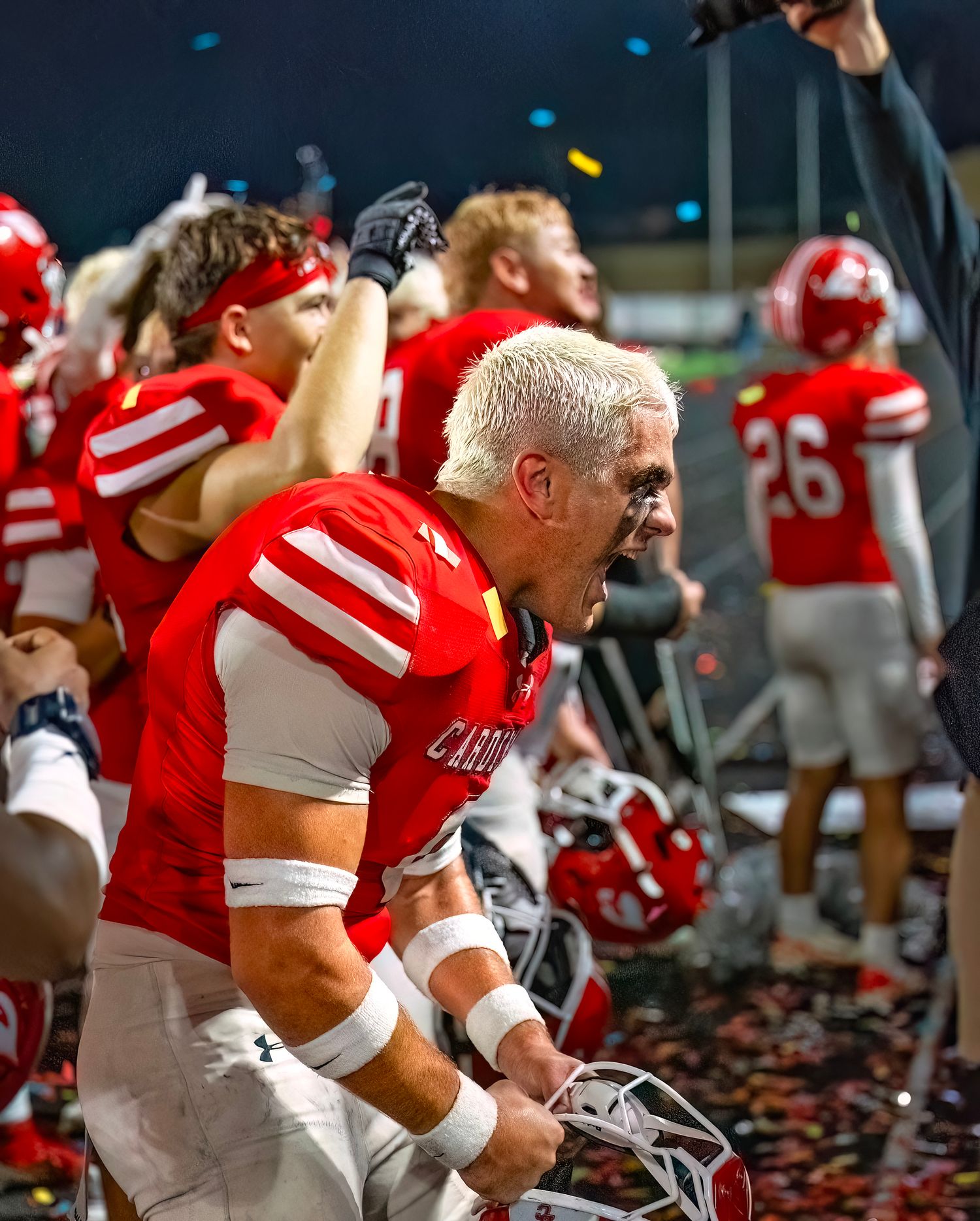 Football players in red jerseys gather on the sidelines during a night game.
