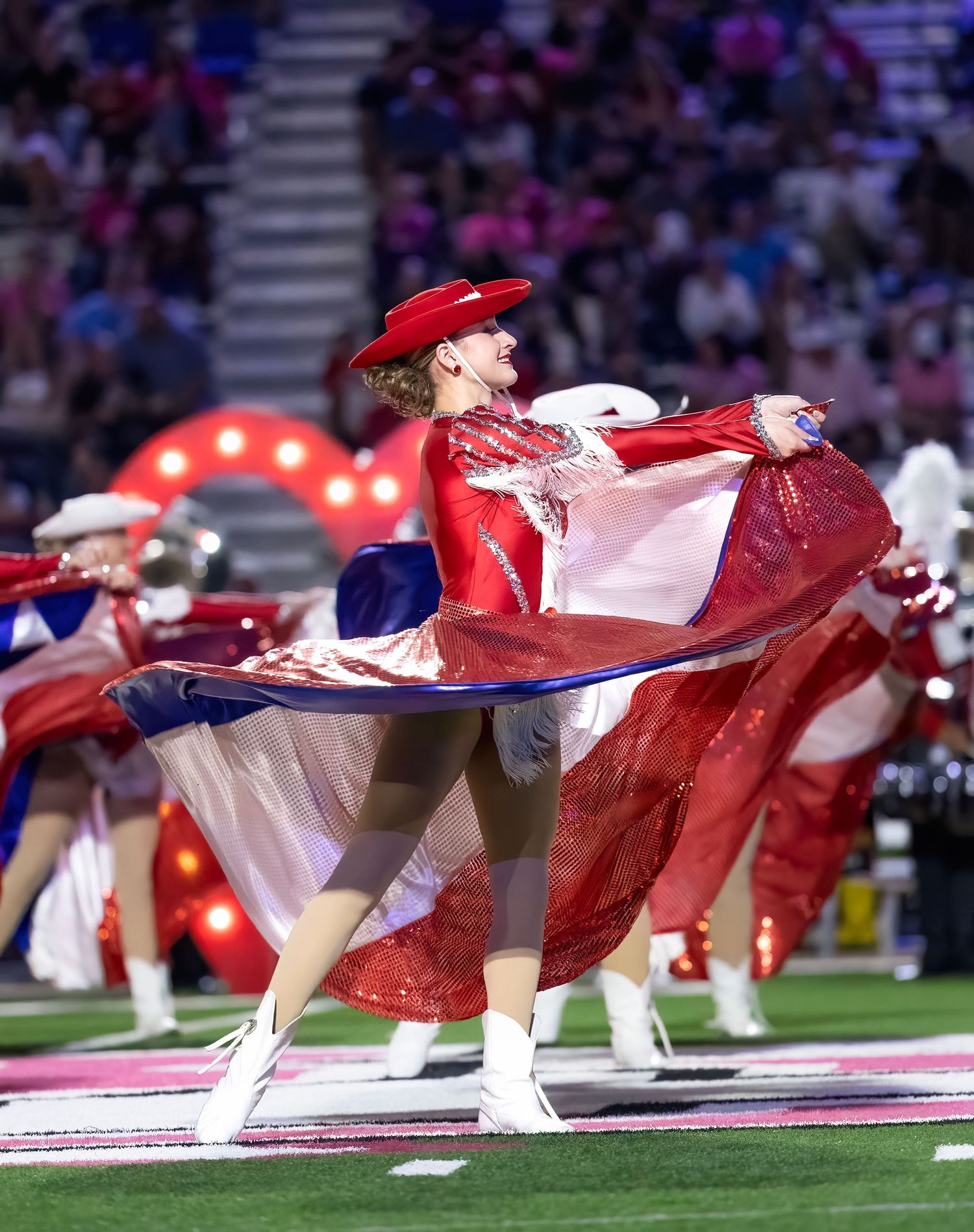 Performers in red and white costumes twirl during a halftime show on a football field.
