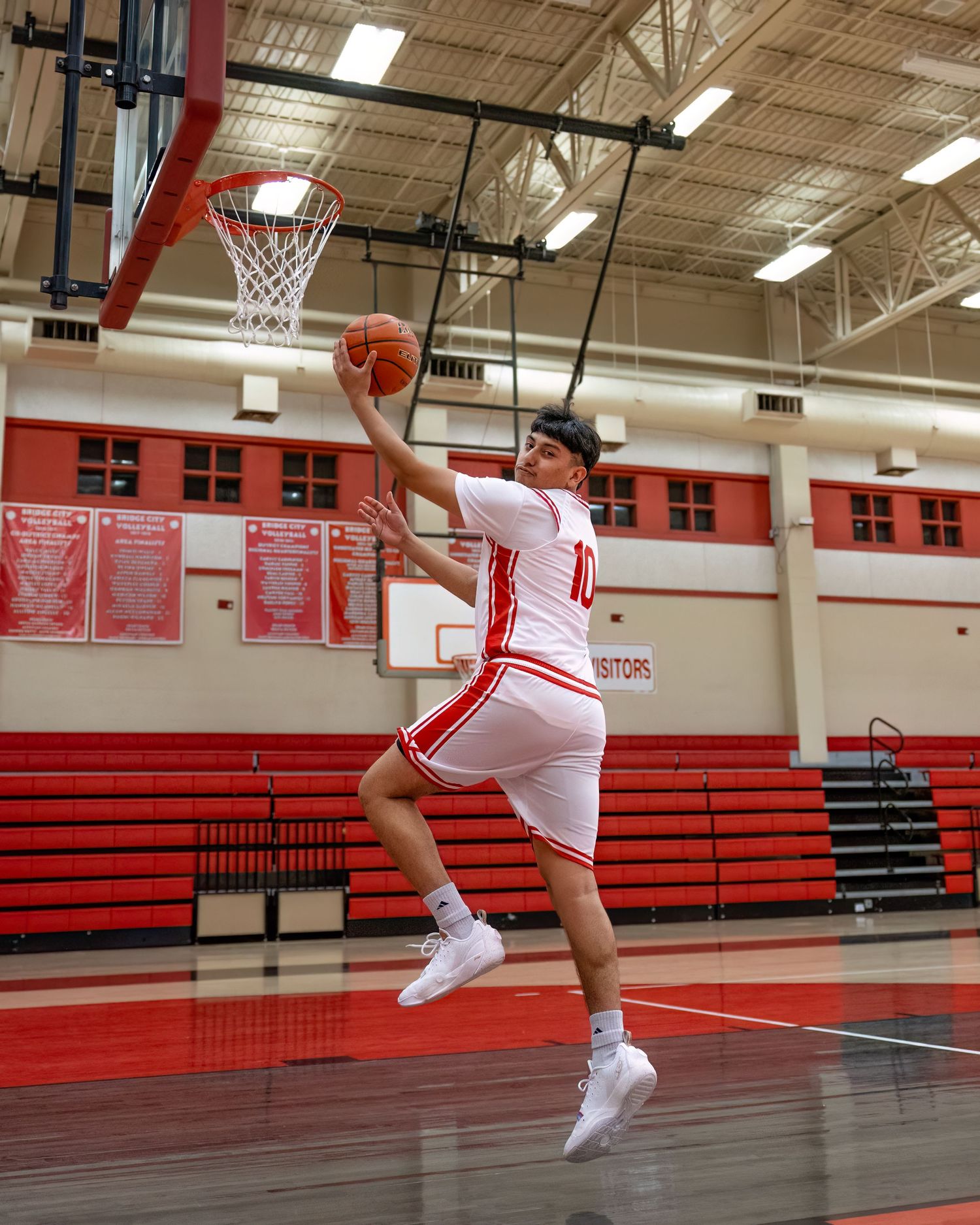 A sequence of basketball jump shots showing progressive motion from takeoff to landing in a high school gymnasium.