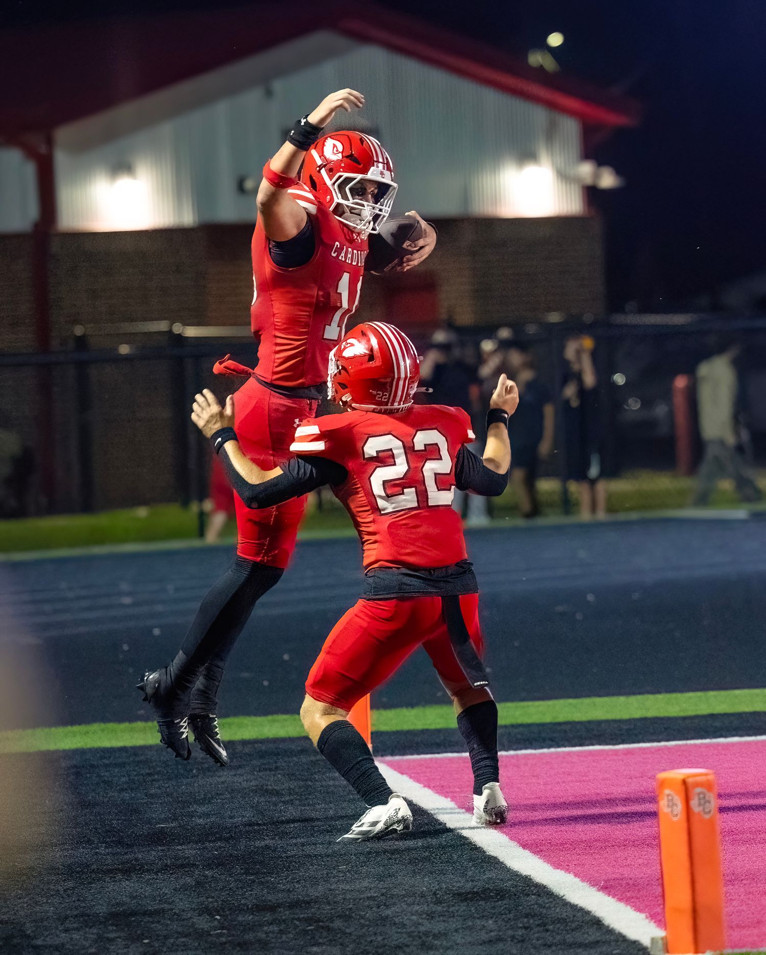 Football player leaps into the end zone while carrying the ball in celebration of touchdown.