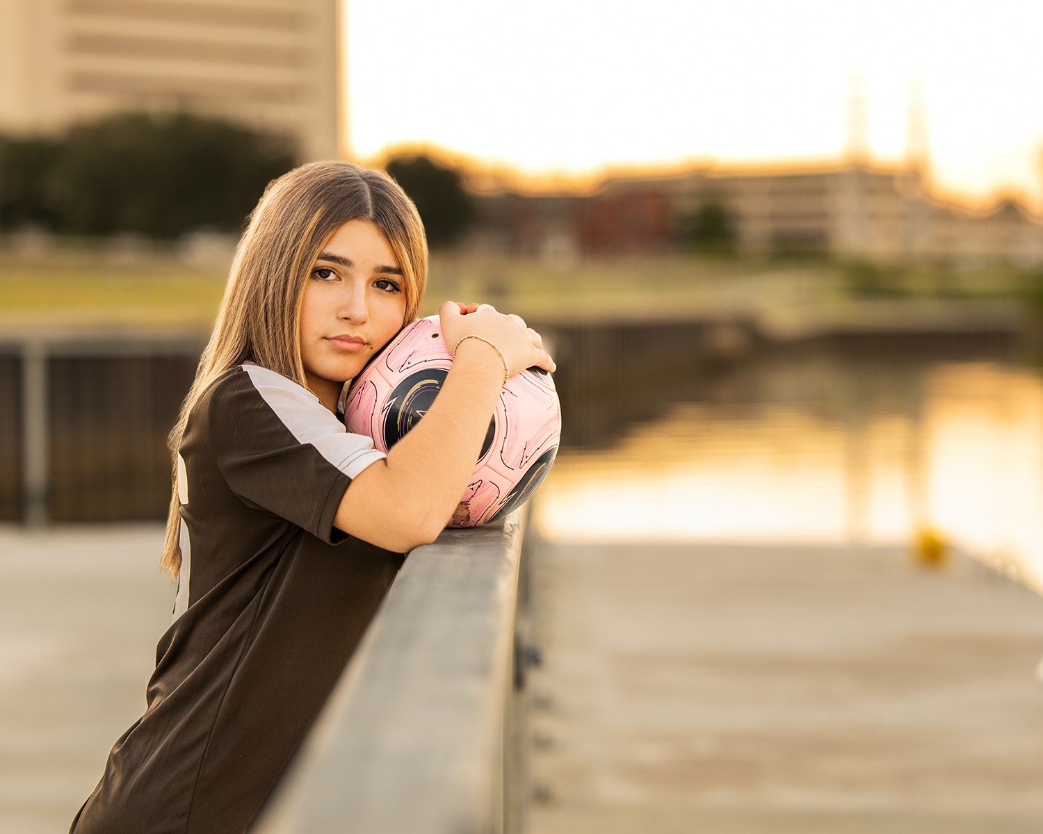 A person in a black top poses against a blurred outdoor background during golden hour sunset.