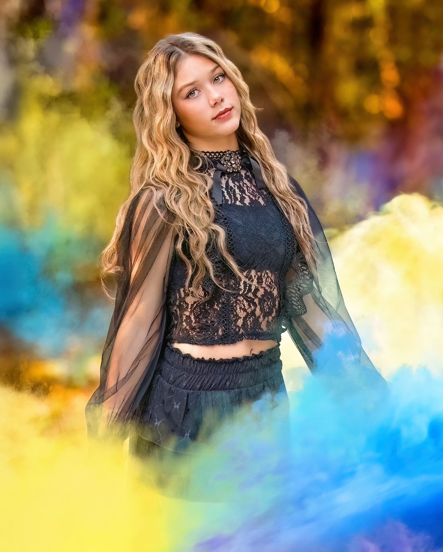 A model in a black lace crop top and sheer sleeves poses against colorful smoke in an autumn setting.