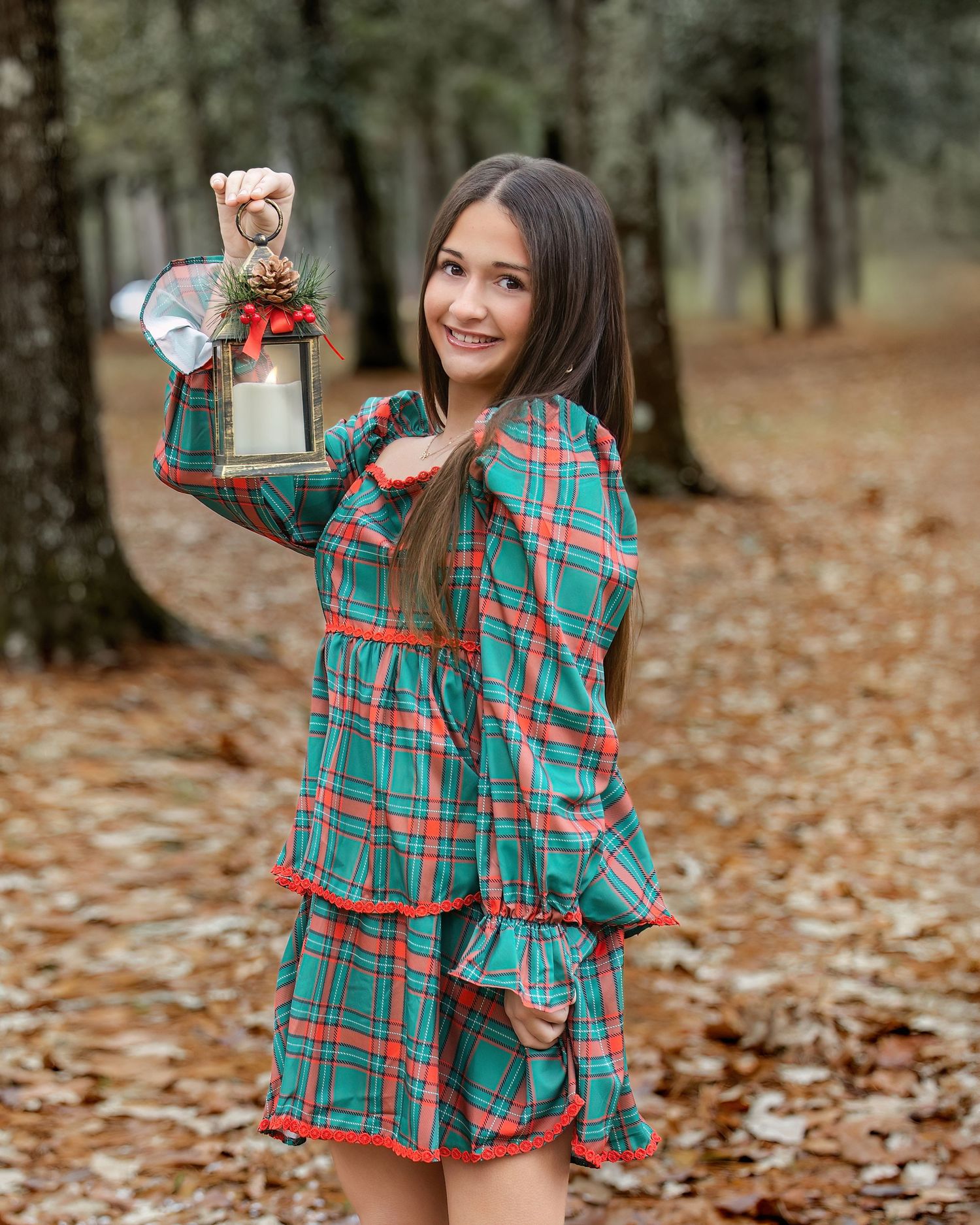 Person in plaid holiday dress twirls with wrapped presents in a forest setting with fallen leaves.