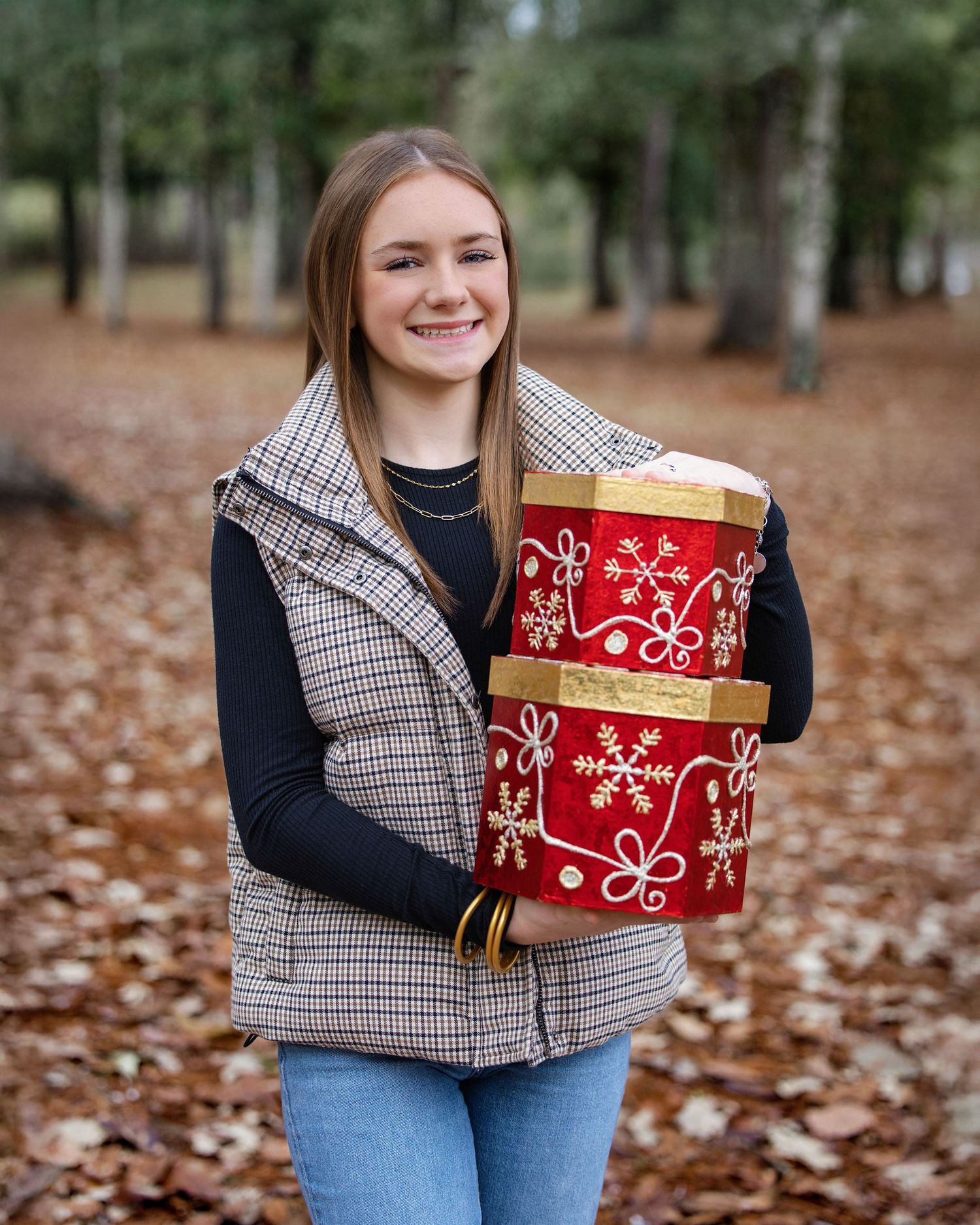 Person wearing plaid vest holds festive red gift boxes outdoors among fallen leaves.