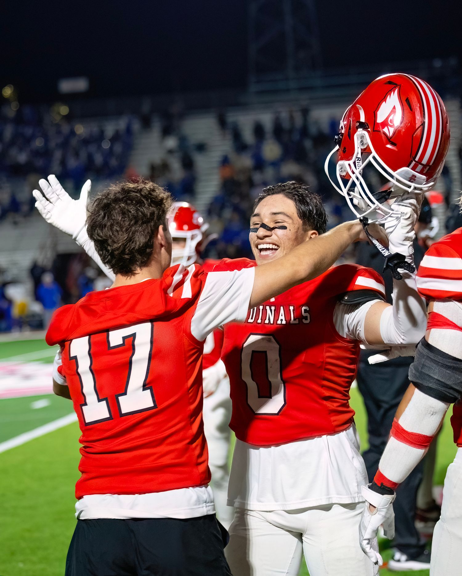 Cardinals football team members embrace and celebrate together on the field.