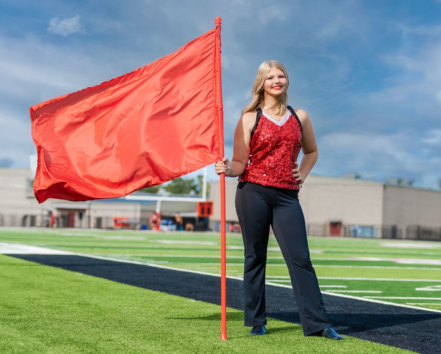 Red flag marker on a green sports field with blue sky and white clouds in the background.