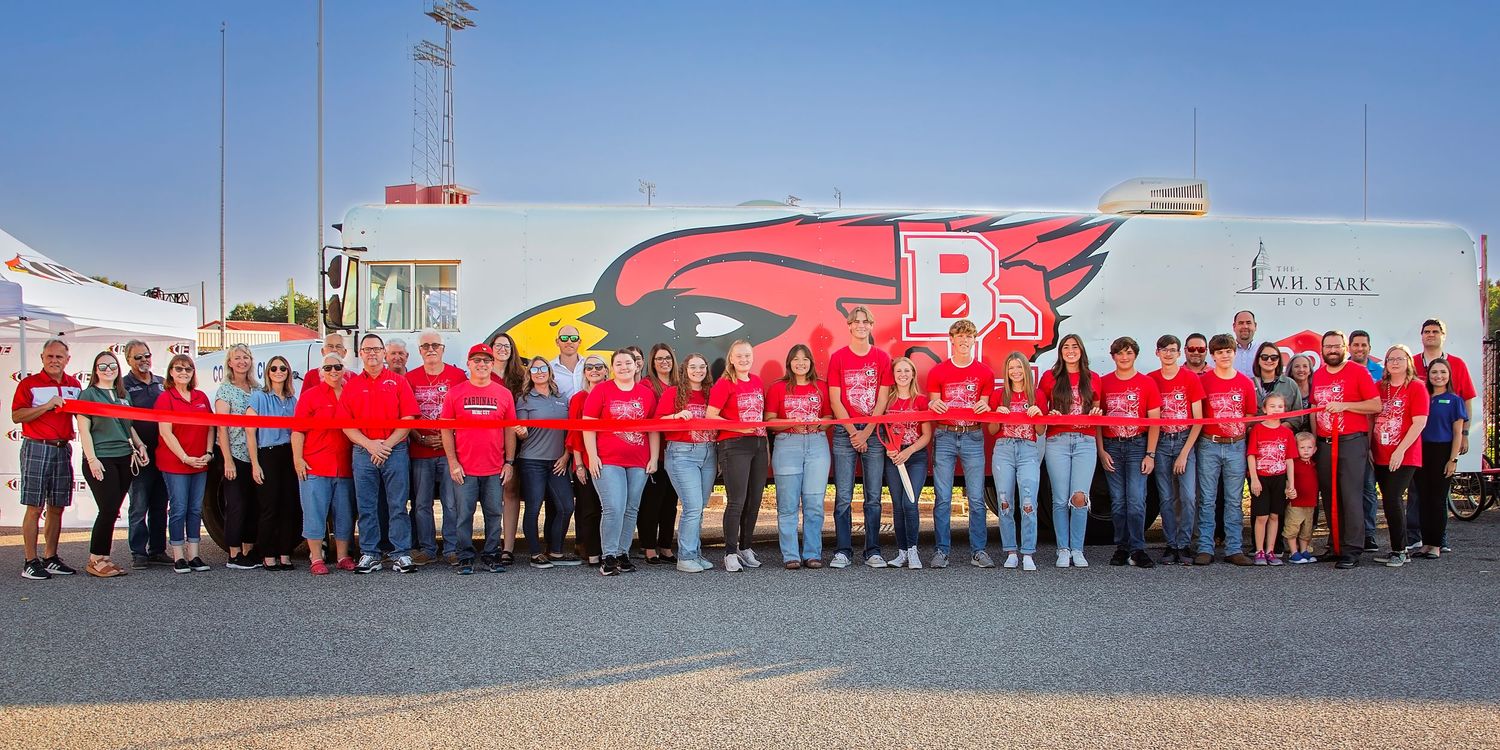 A panoramic view Bridge City Stem bus ribbon cutting outdoors in multiple groups against a light background.