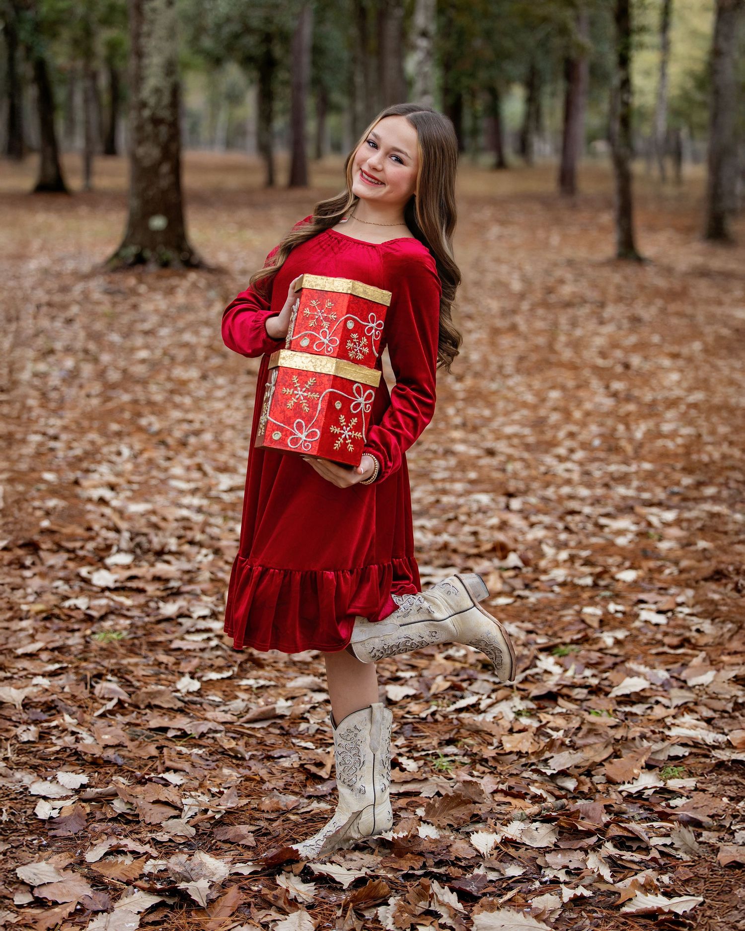 Festive holiday portrait in a red velvet dress holding Christmas gift boxes among fallen autumn leaves.