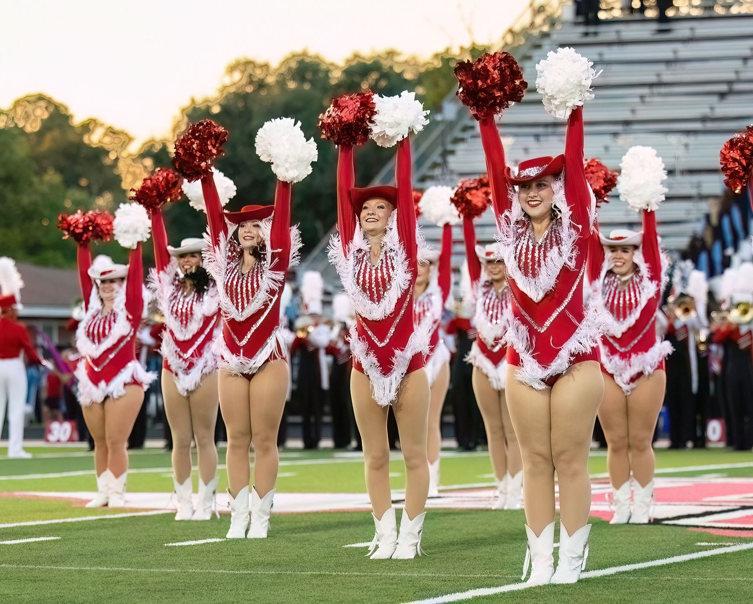 Cheerleaders in red and white uniforms perform a synchronized dance routine on a football field during a game.
