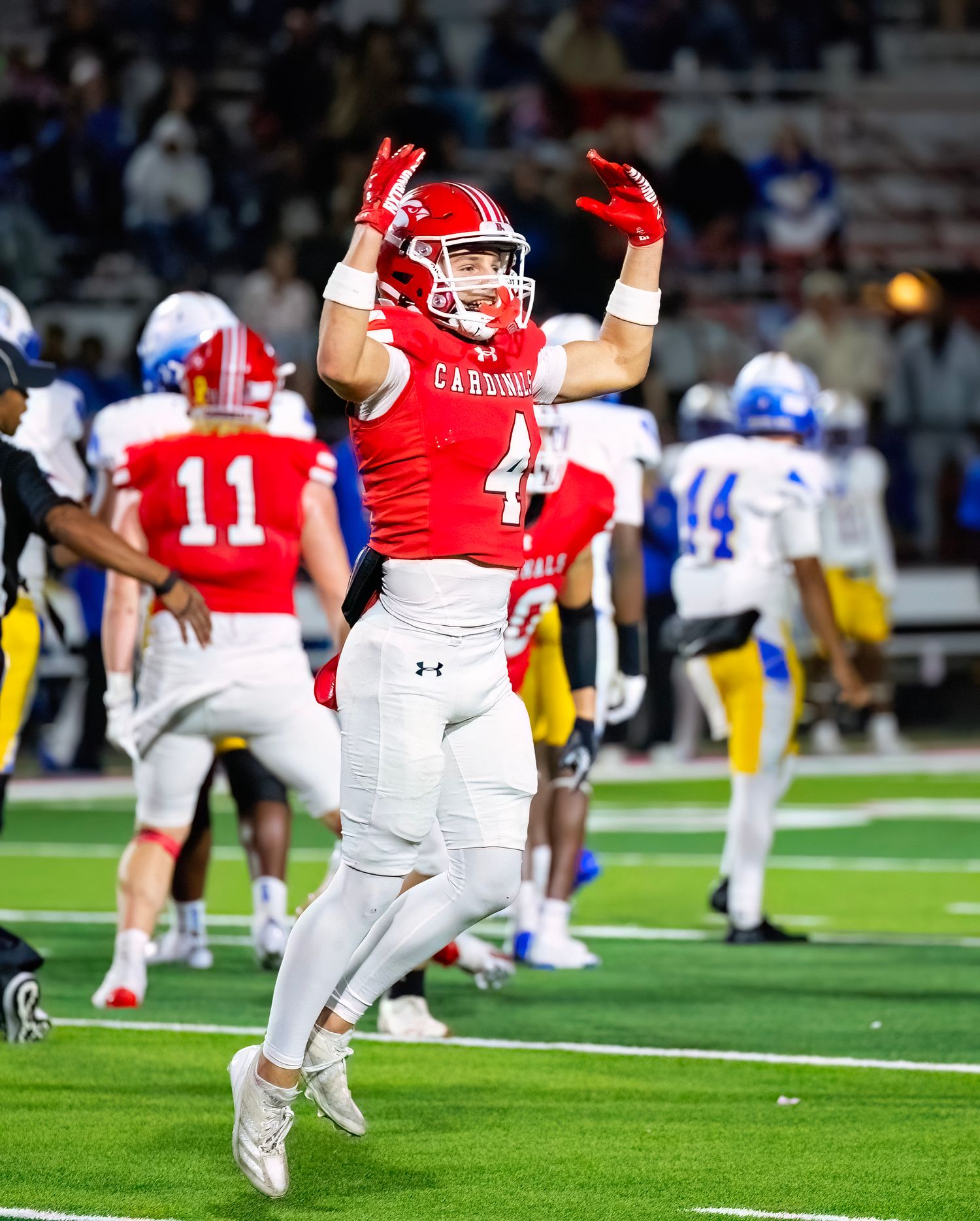 Football players in red and white uniforms celebrate on the field during a night game.