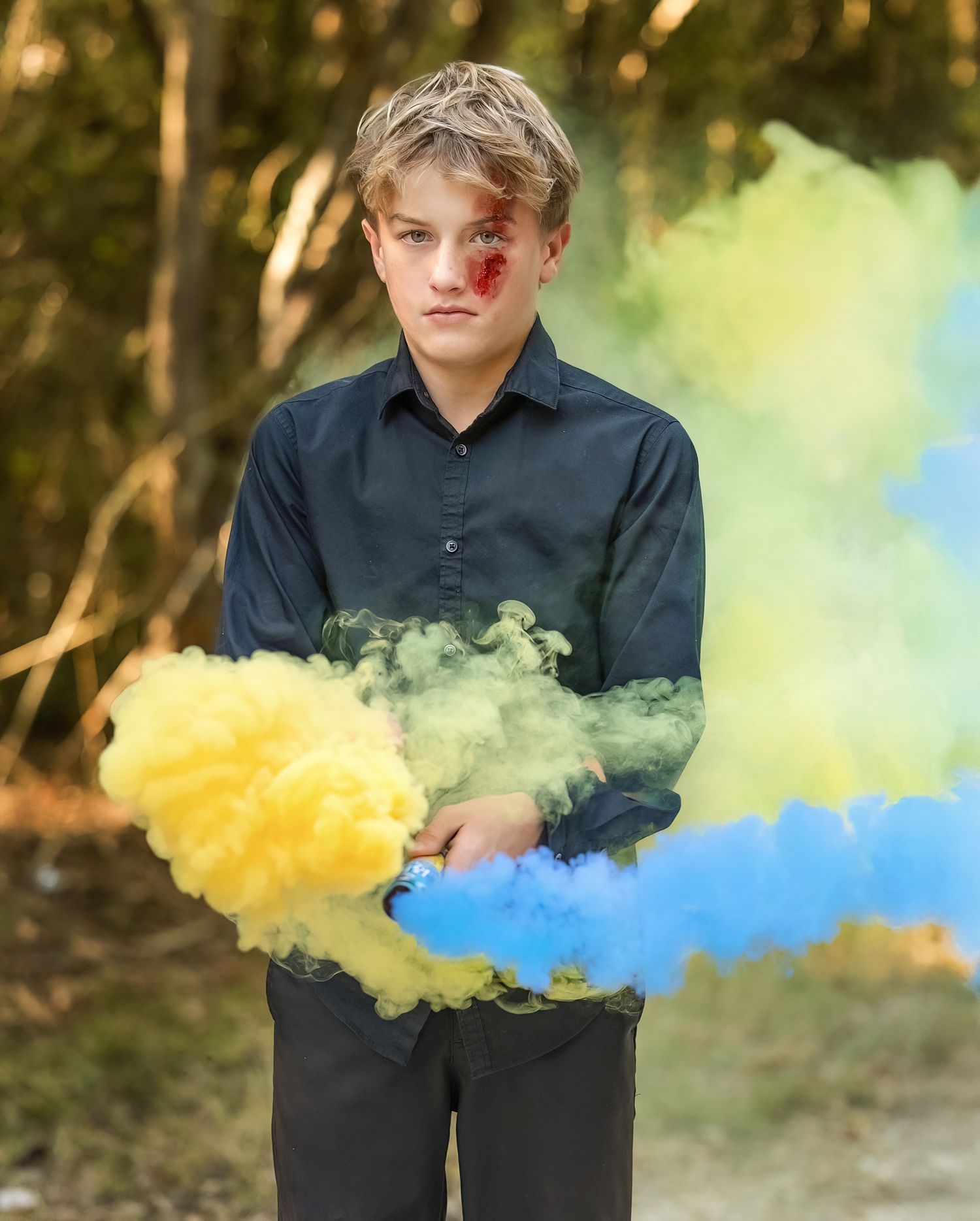 Creative portrait with yellow and blue smoke bombs creating a colorful effect in a wooded setting.