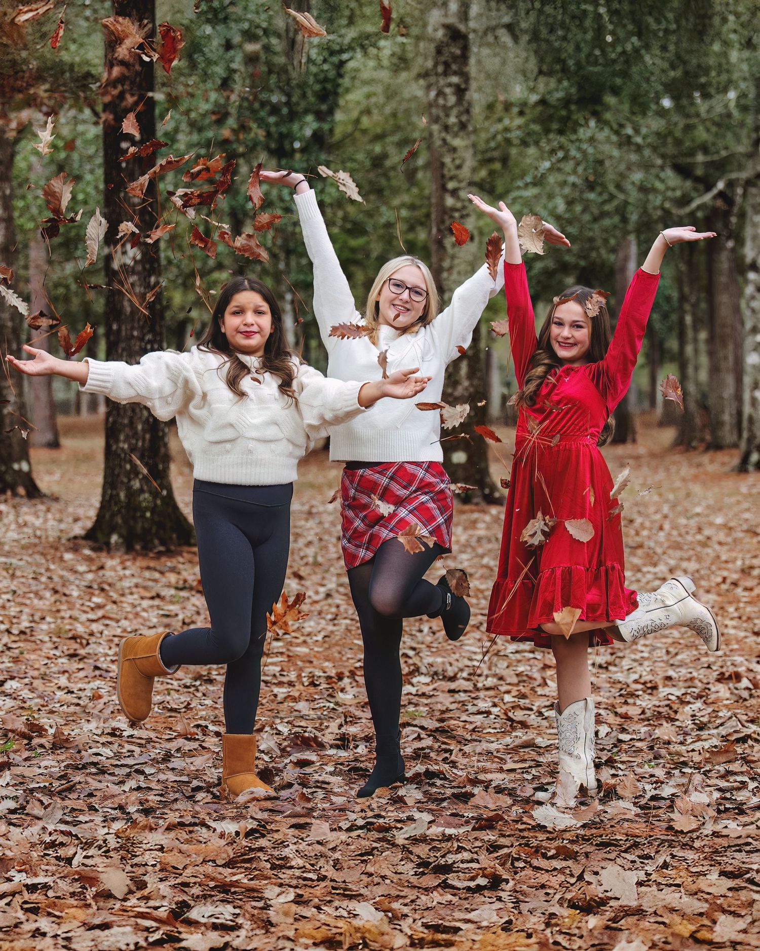 Model Team with Three friends playing and throwing autumn leaves in a wooded area during a fall photoshoot.