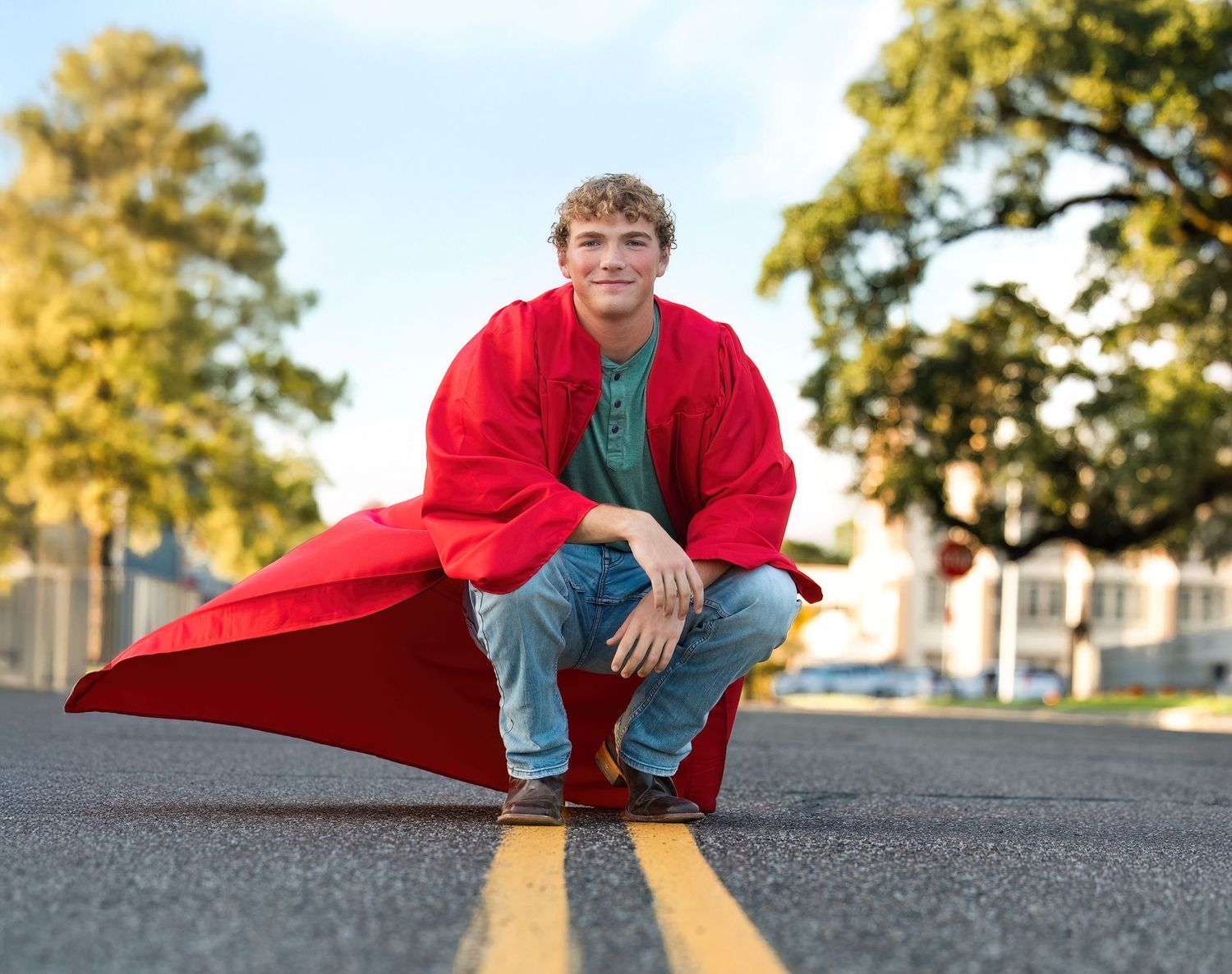 A person in a red sweater sits on a concrete surface during golden hour as sunlight casts long shadows.