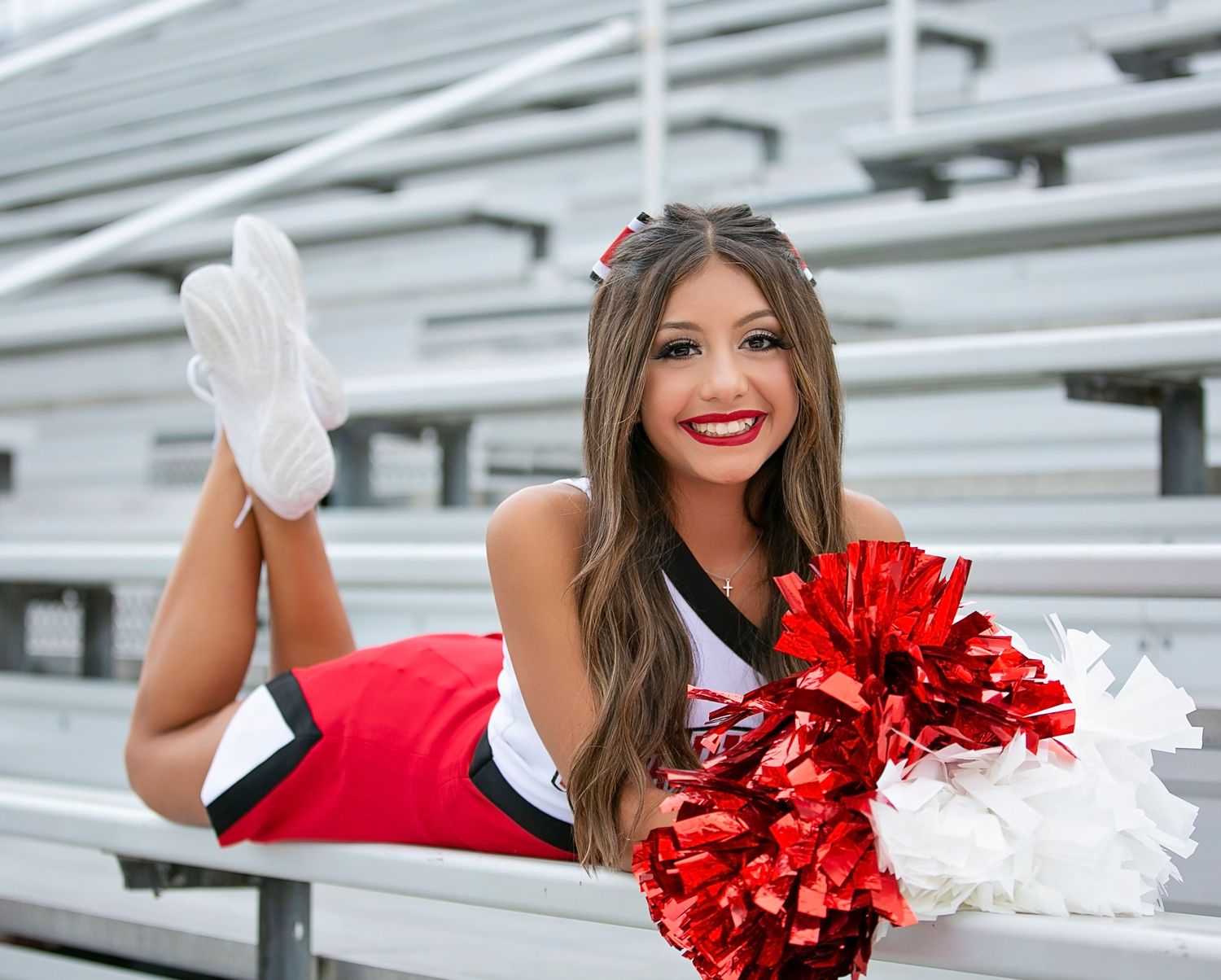 A cheerleader in red uniform performs a dynamic pose sequence on bleachers with red and white pom poms.