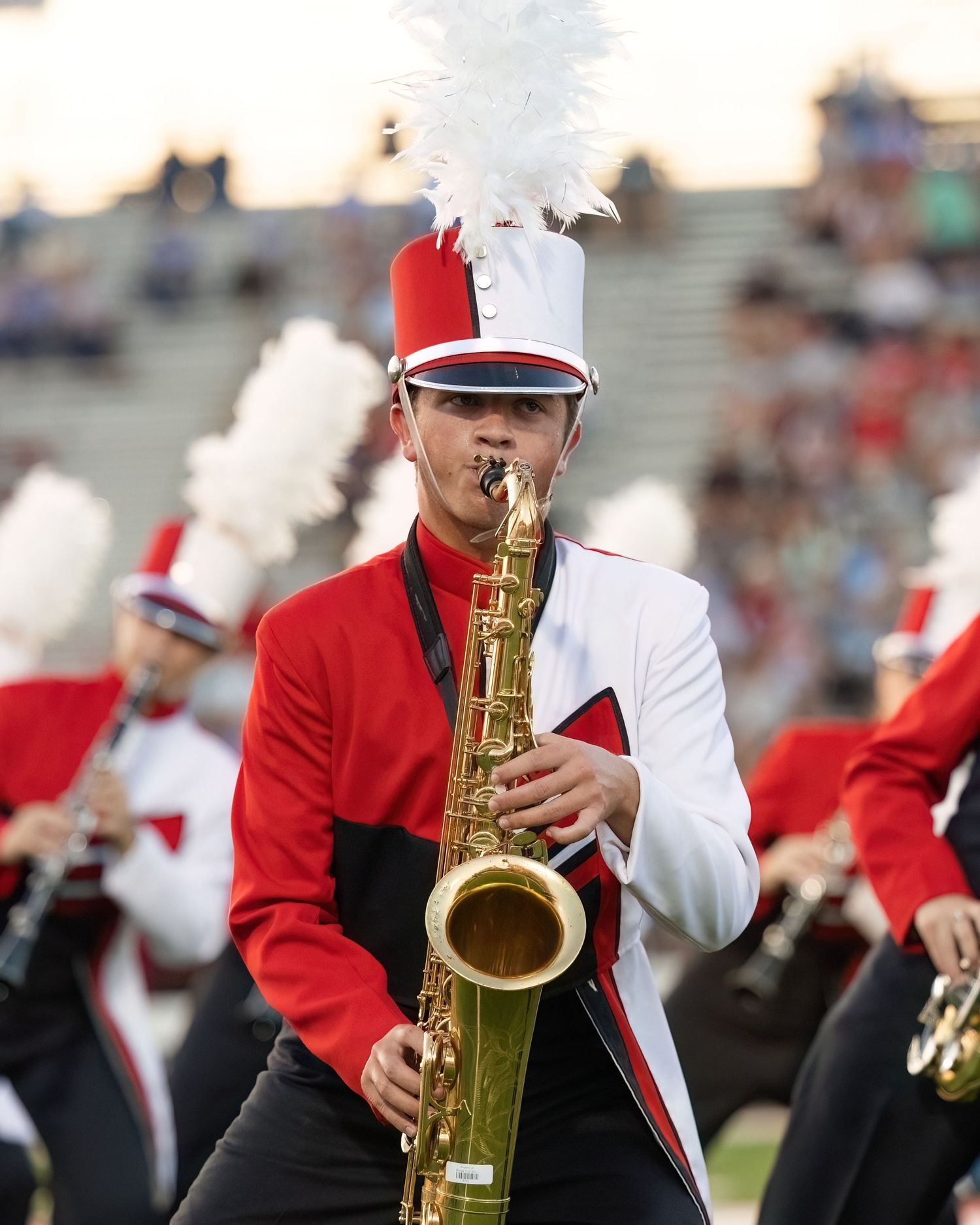 Marching band members in red uniforms play brass instruments during a football game performance.