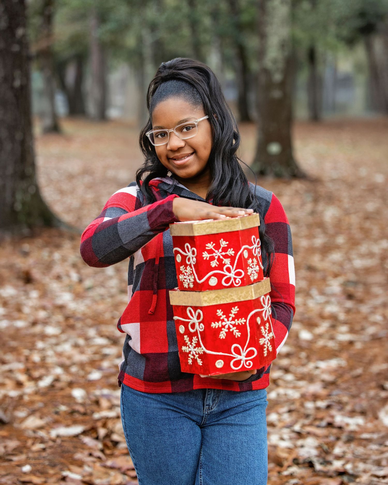 Casual winter portrait with buffalo plaid shirt holding red decorative Christmas boxes in a forest setting.