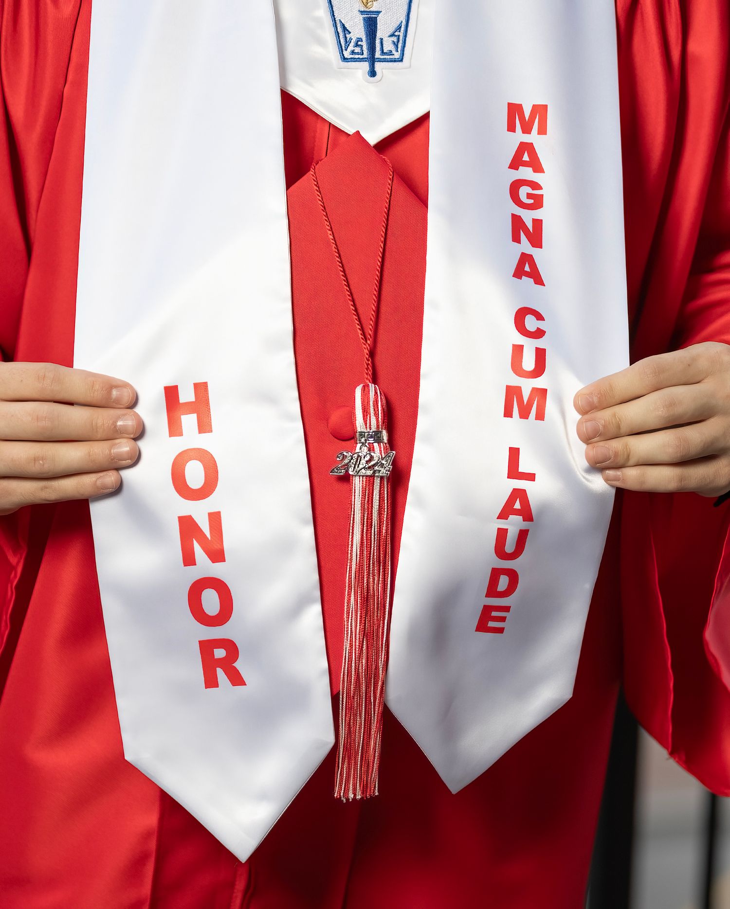 Graduates in red gowns hold white stoles with red text during a commencement ceremony.