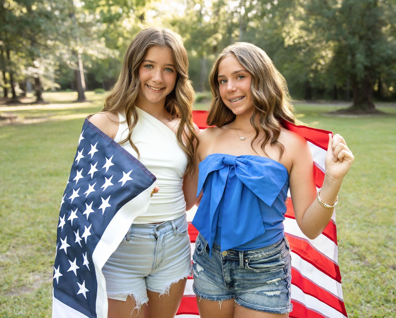 Two people pose with American flag in outdoor summer setting wearing casual denim and white tops.