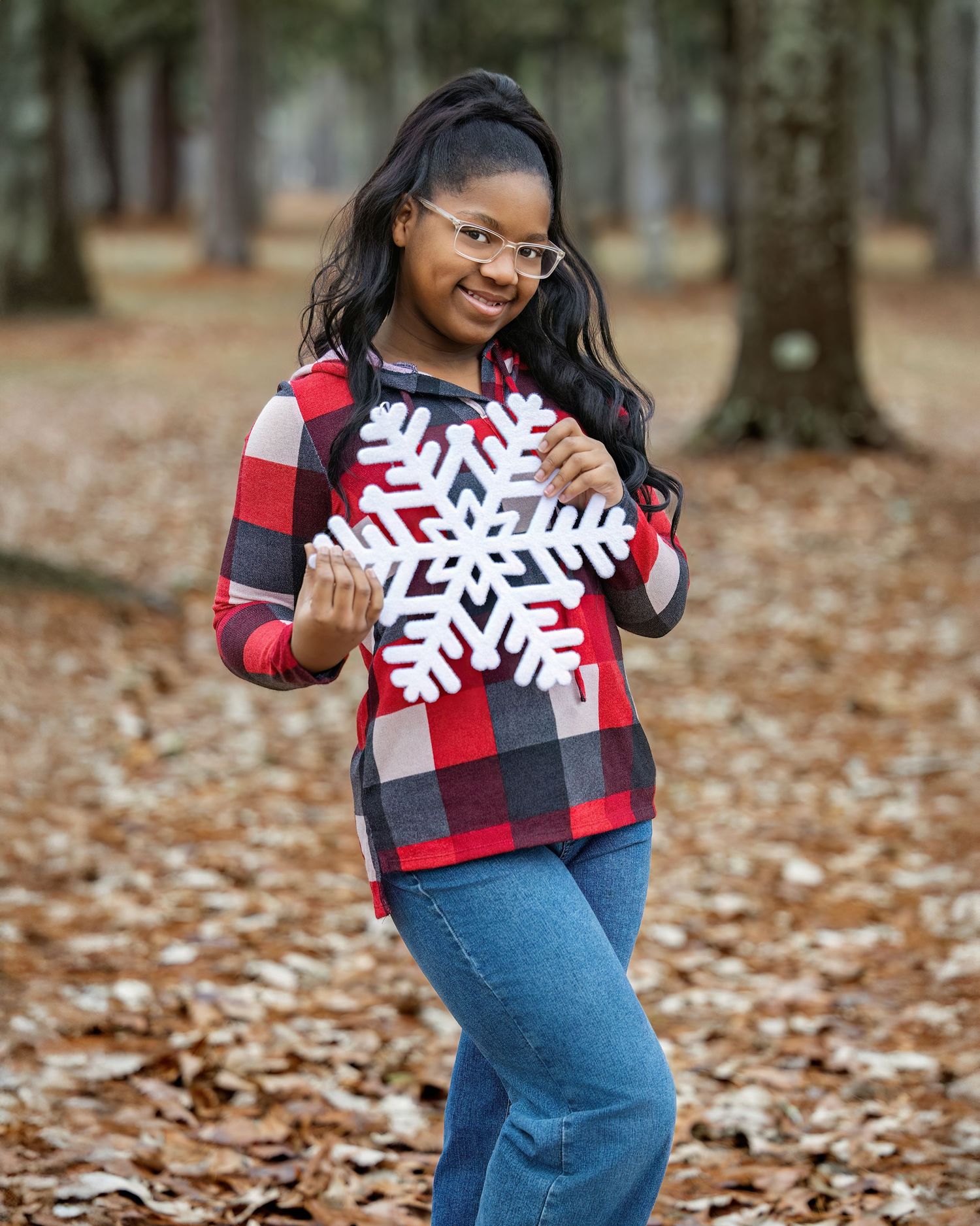 Woman in buffalo plaid sweater with snowflake design poses outdoors among fallen leaves.