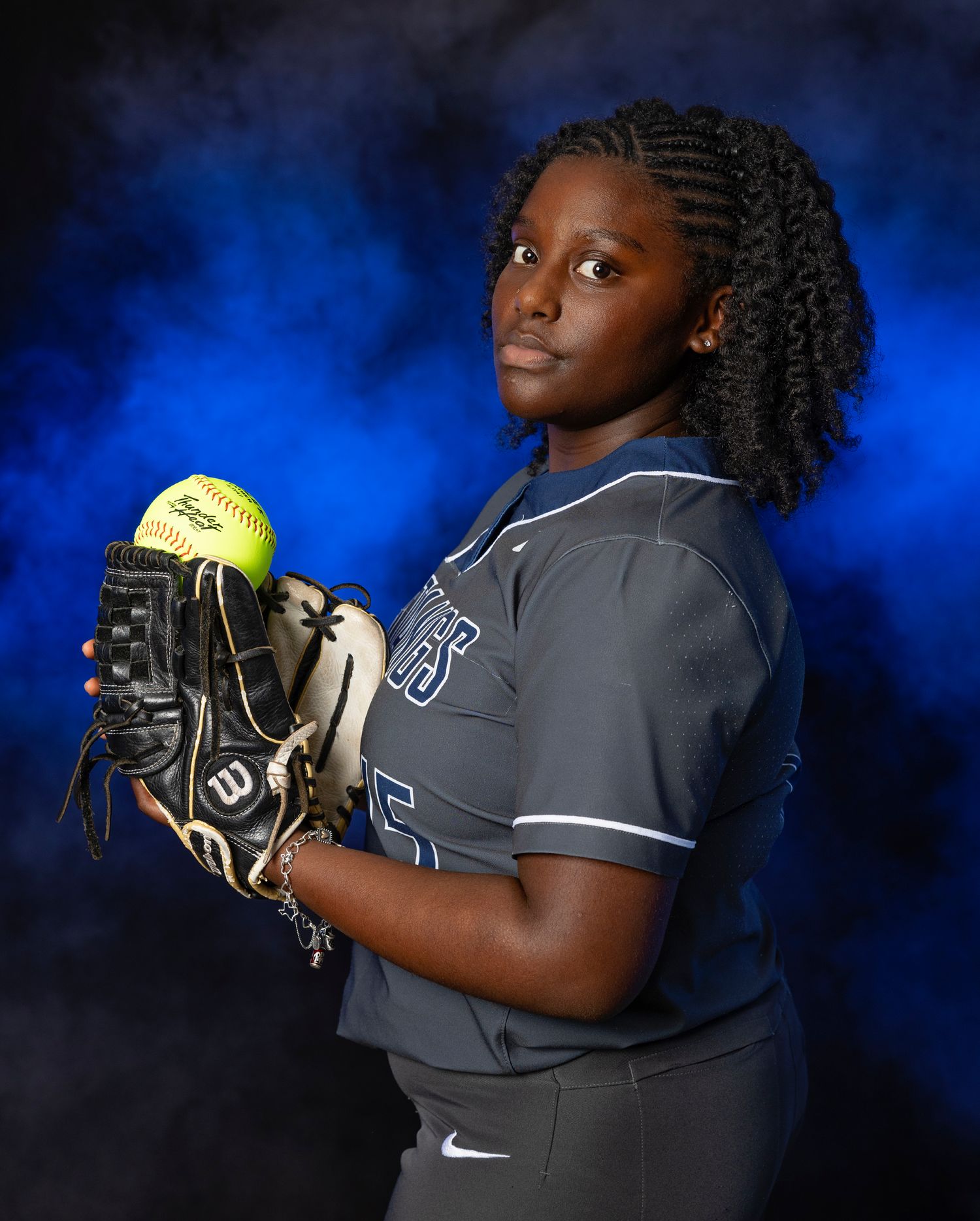 Softball player in grey uniform holds yellow ball against dramatic blue backdrop in series of action poses.