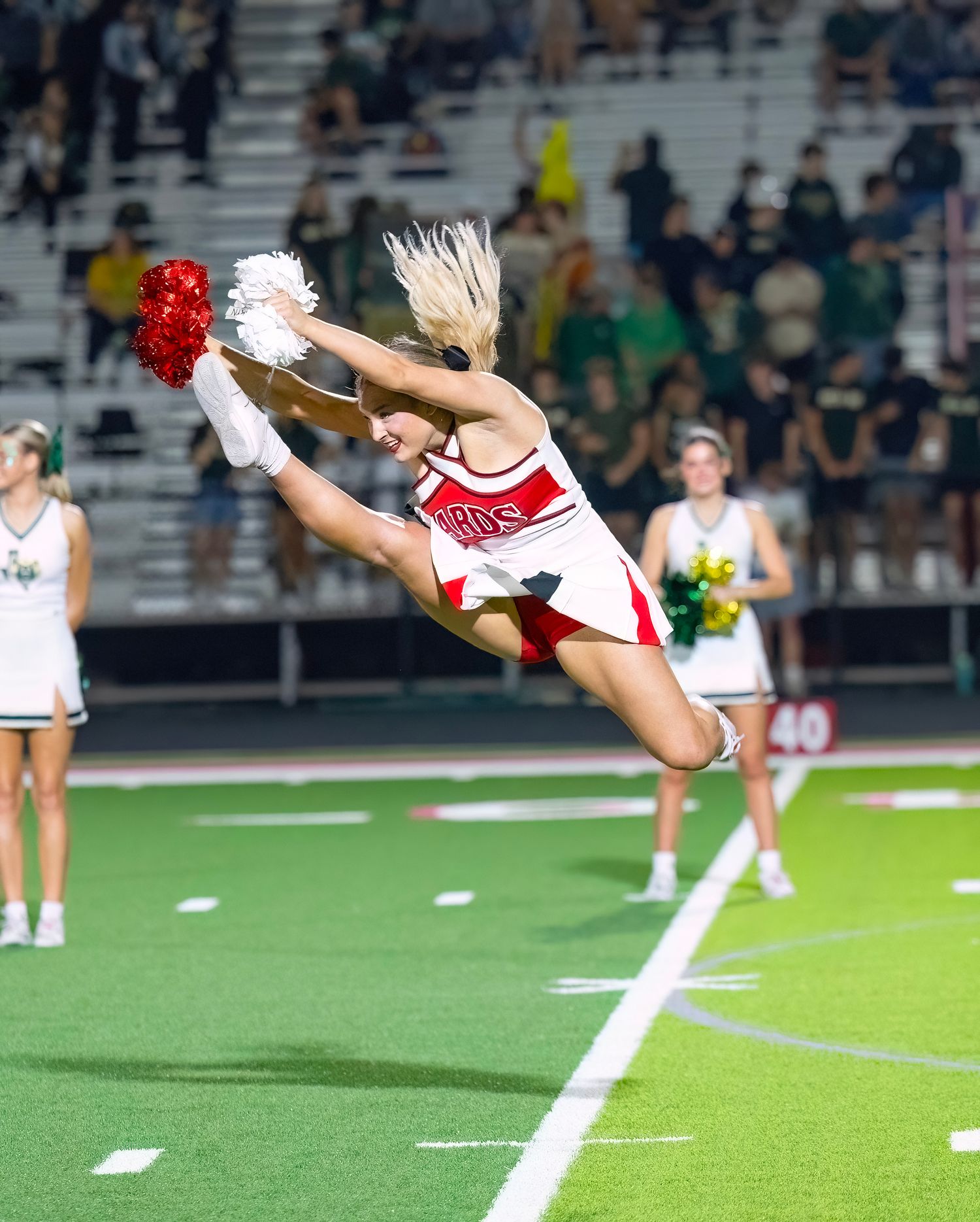 Cheerleaders perform high-energy acrobatic stunts on a football field during a game.