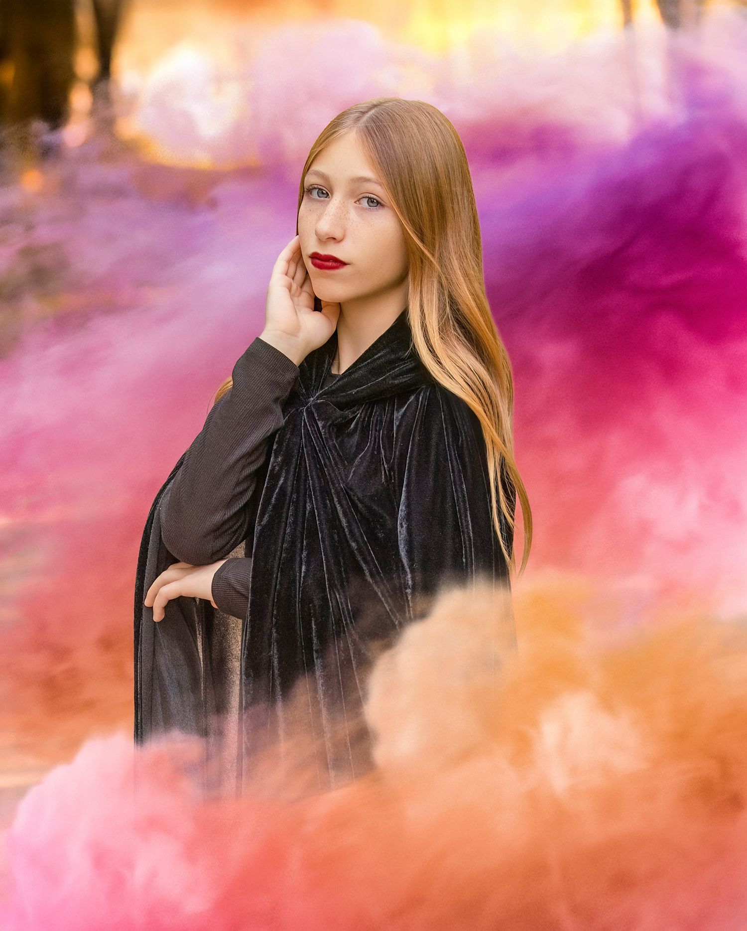 Moody portrait in a black velvet cape surrounded by colorful smoke effects in pink and orange.