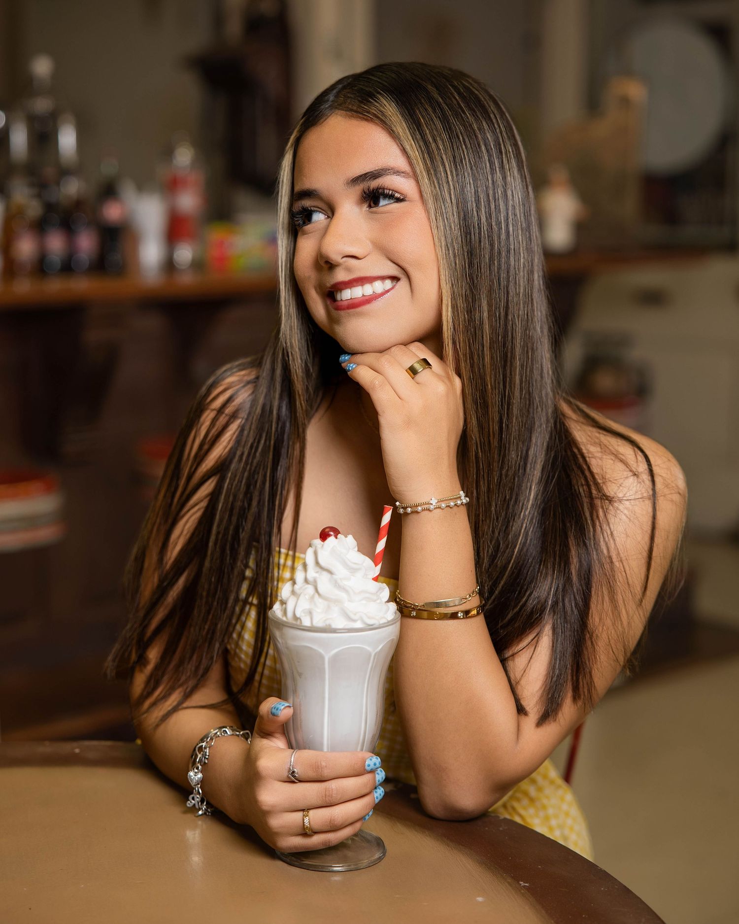 Person with long dark hair enjoying a whipped cream topped drink while sitting at a table.