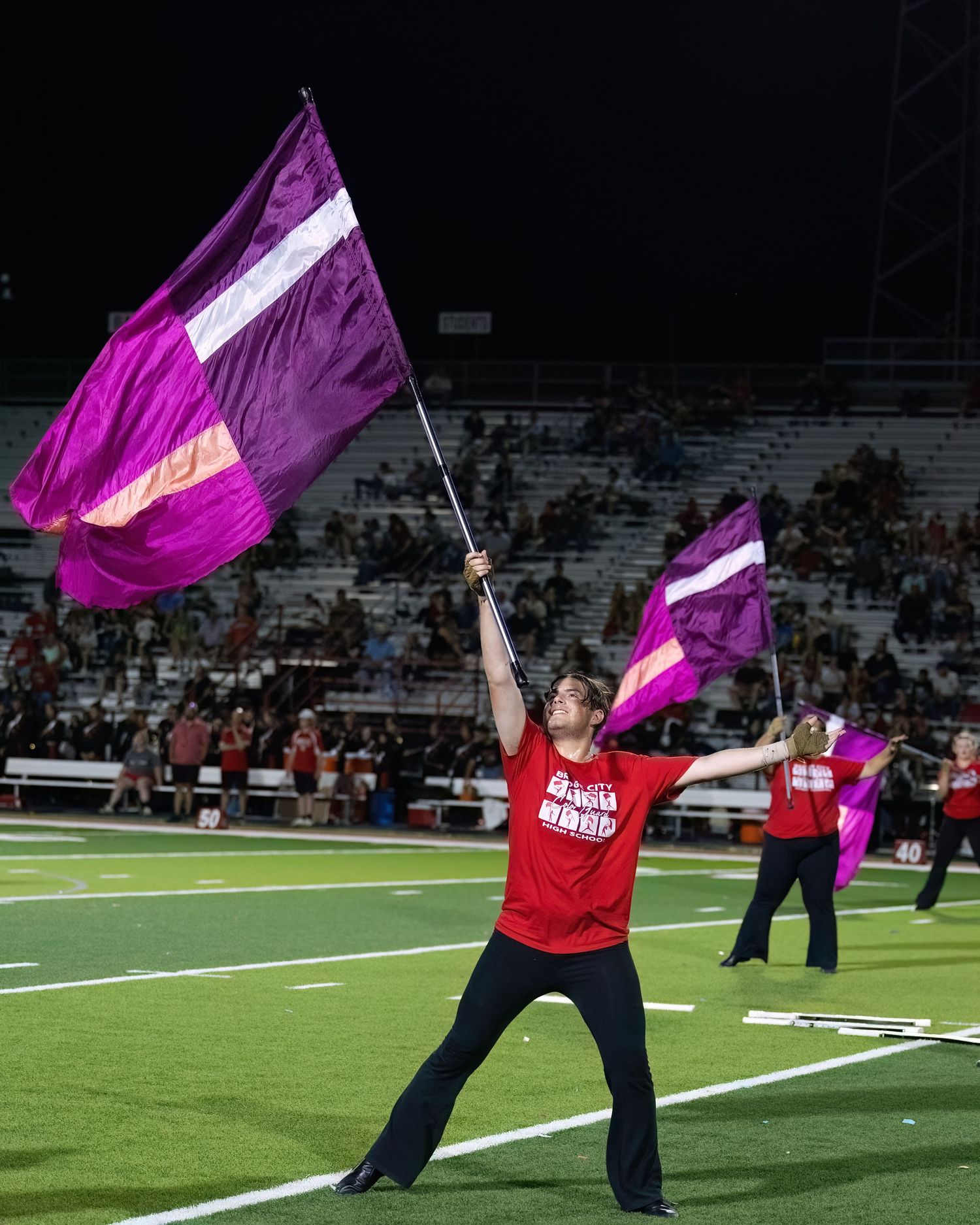 Color guard member waves large purple and white flags during halftime performance on football field.
