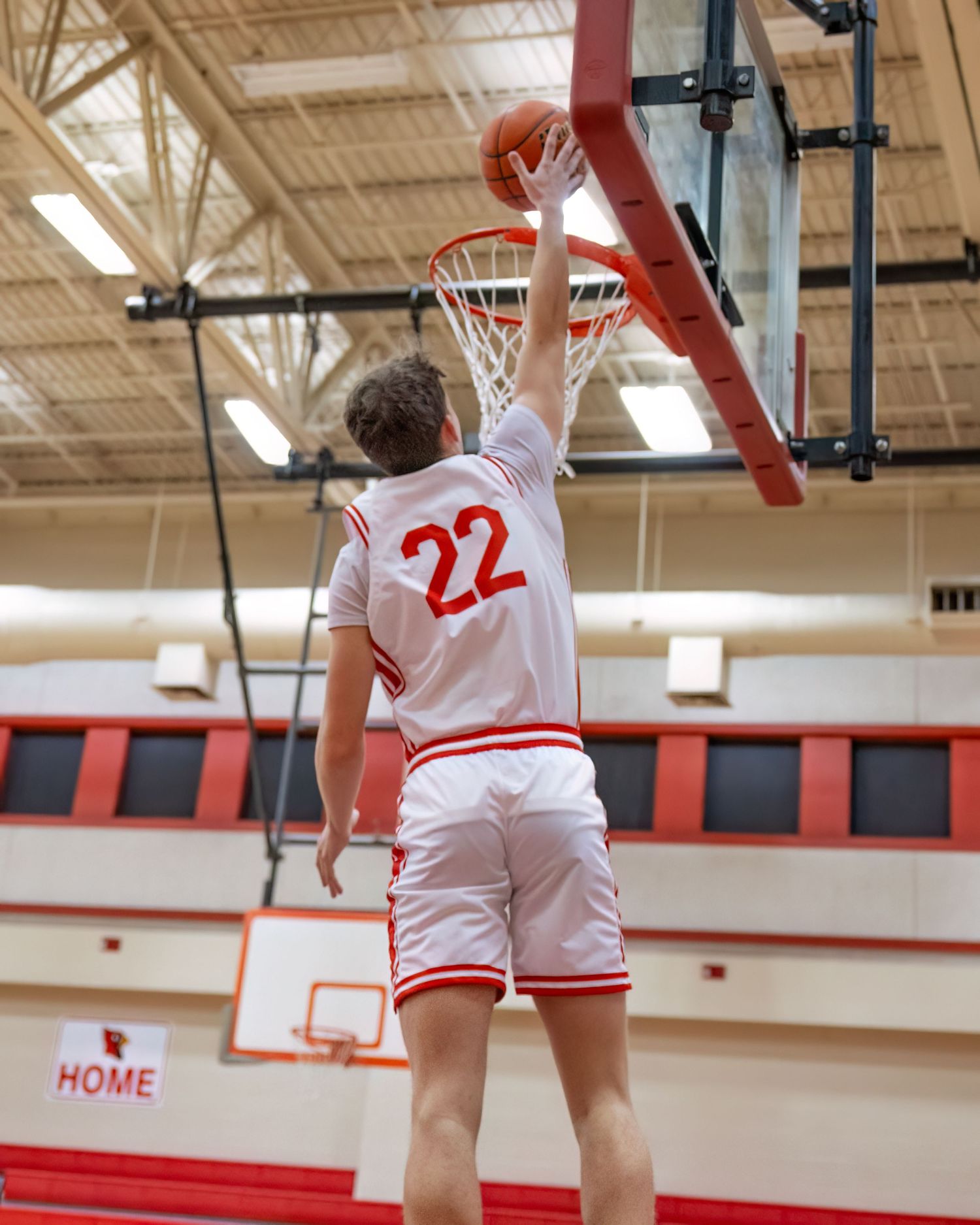 Basketball player in white jersey number 22 jumps high for a slam dunk in a school gymnasium.