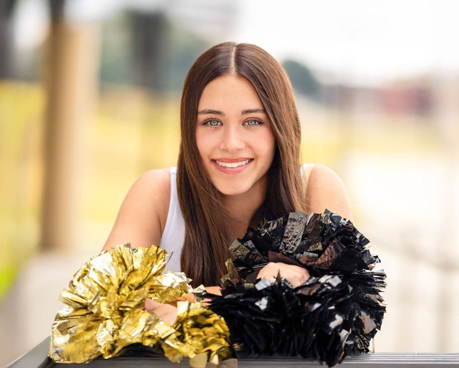 Vidor cheerleader in a black outfit poses with gold and black pom poms outdoors on a sunny day.