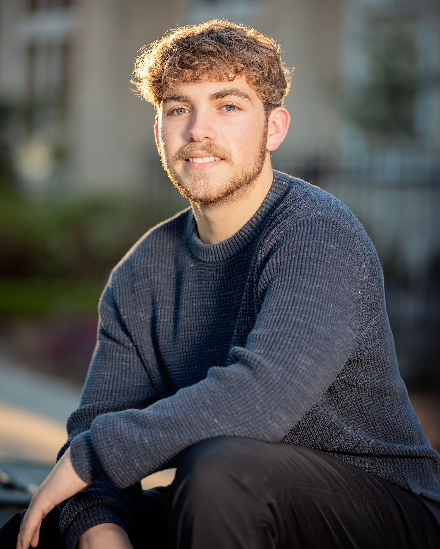A person in a navy knit sweater sits outdoors with a thoughtful expression during golden hour lighting.
