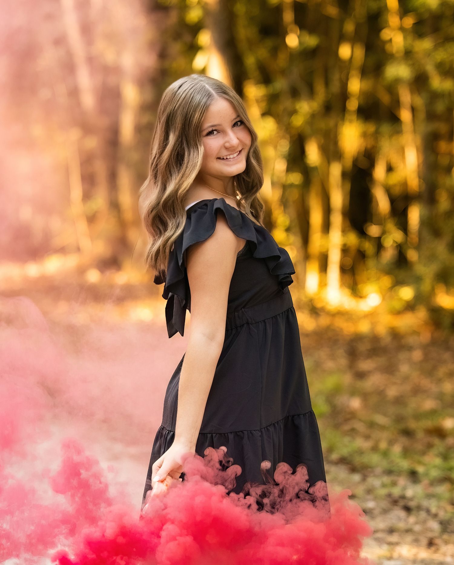 A black dress stands out against a natural woodland backdrop with pink smoke effects.