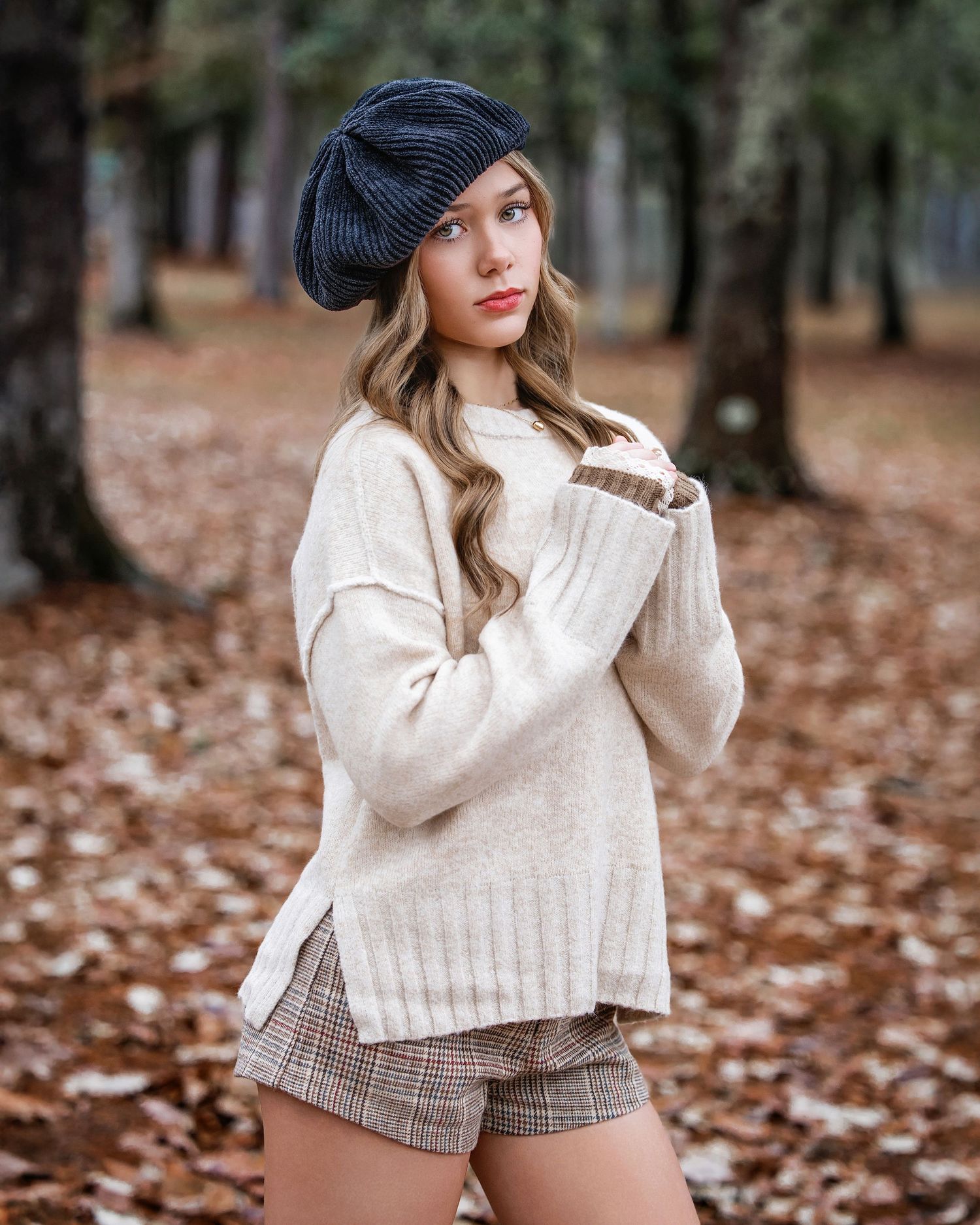 Fall fashion portrait with cream sweater, plaid shorts and navy beret among fallen leaves.