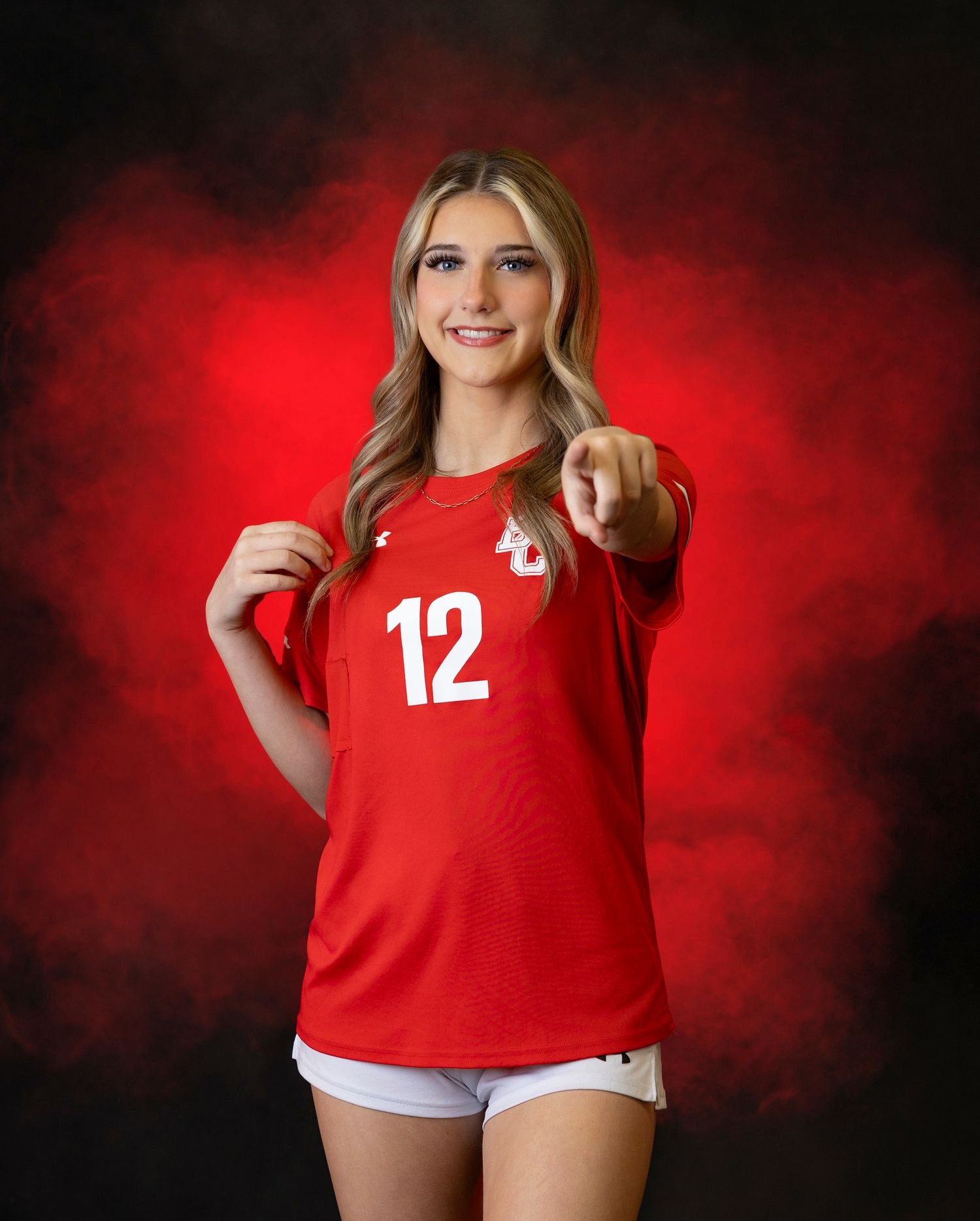 Athletic player in red jersey number 12 poses for portrait against dramatic red smoke background.