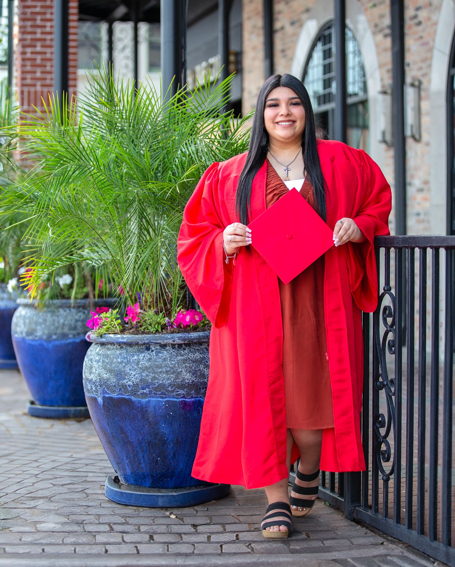 A series of photos showing graduates in bright red gowns posing near blue planters and brick buildings.