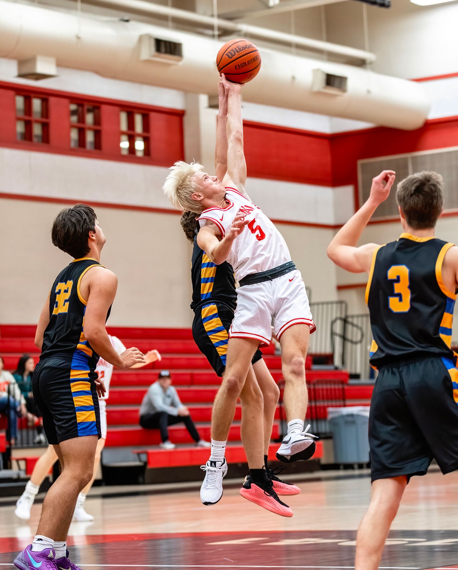 Basketball player in white jersey leaps high to block a shot during an intense game against navy-uniformed opponents.