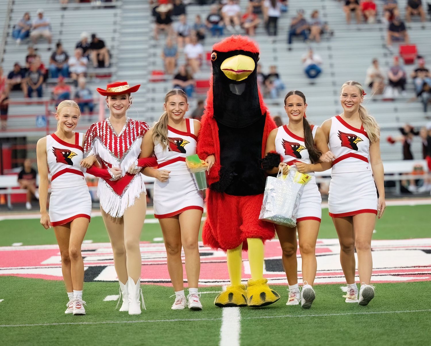 College cheerleaders in red and white uniforms perform a synchronized routine on a football field during a game.