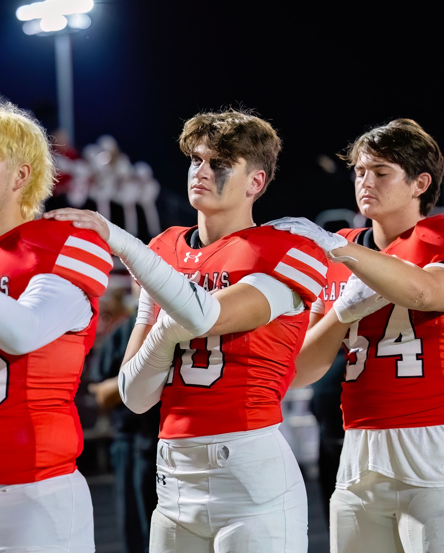 Football players in red and white uniforms stand in formation on the field at night.